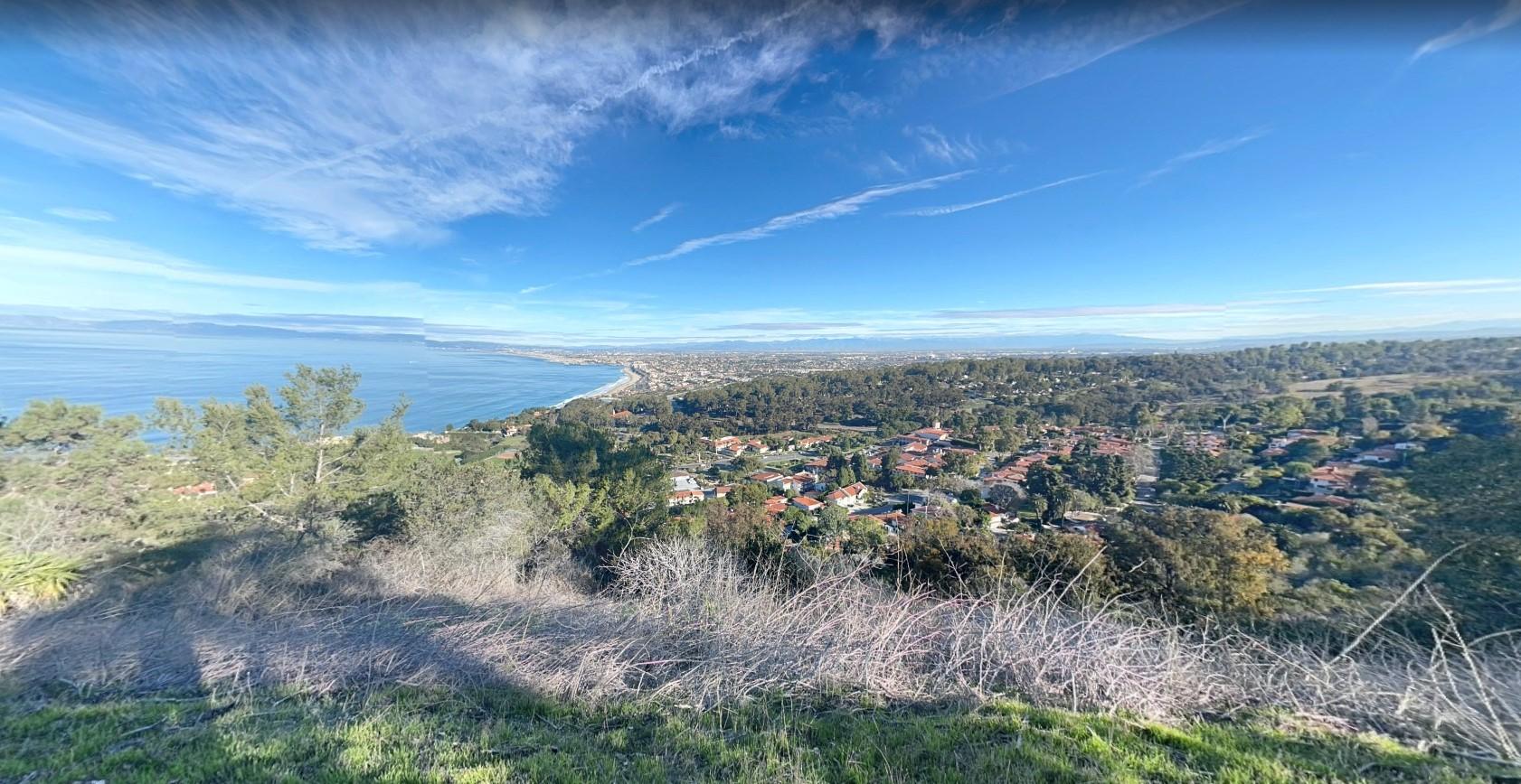 Panoramic sunny view of a coastal town, ocean, and distant hills.