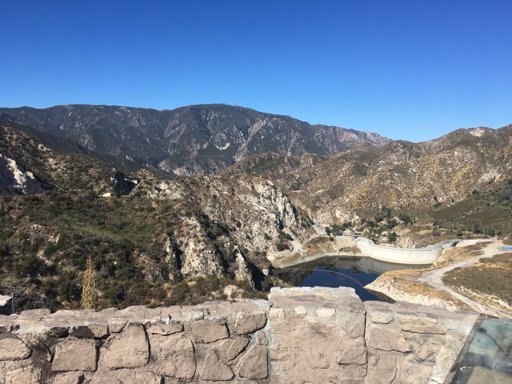 Panoramic view of a reservoir nestled among rugged mountains under a clear sky.