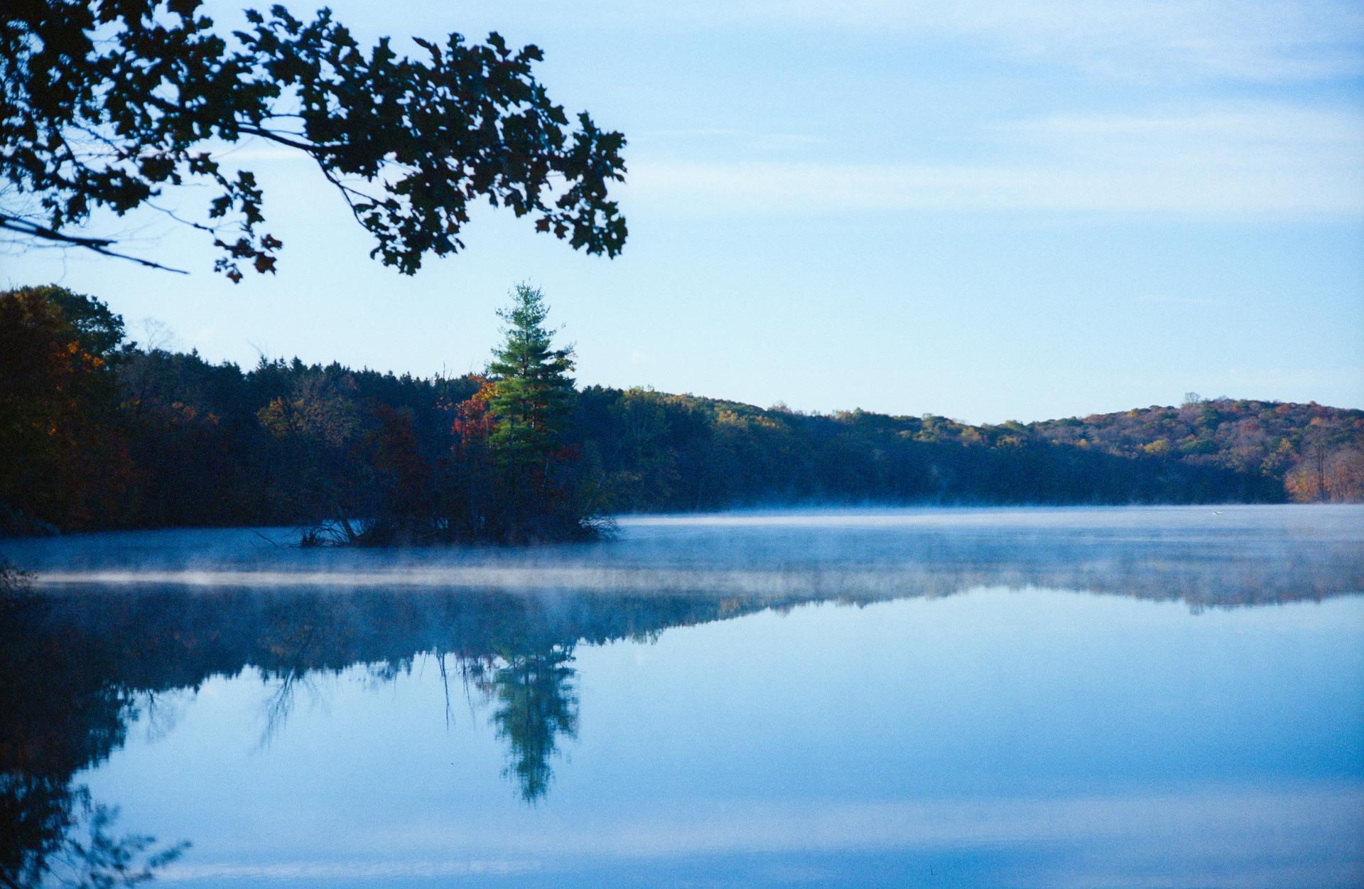 Misty lake reflecting a clear sky, surrounded by autumn trees.