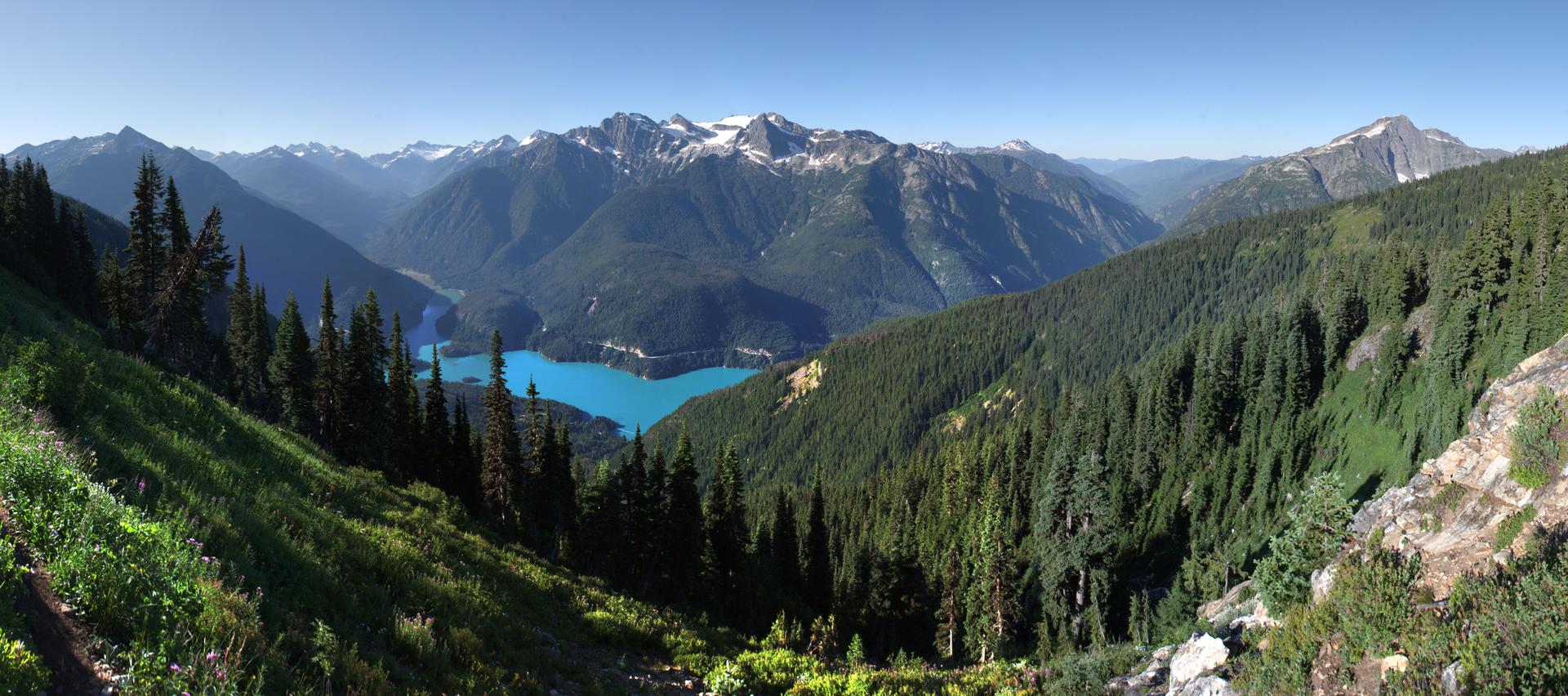 Panoramic mountain valley with a bright turquoise lake under a clear sky.