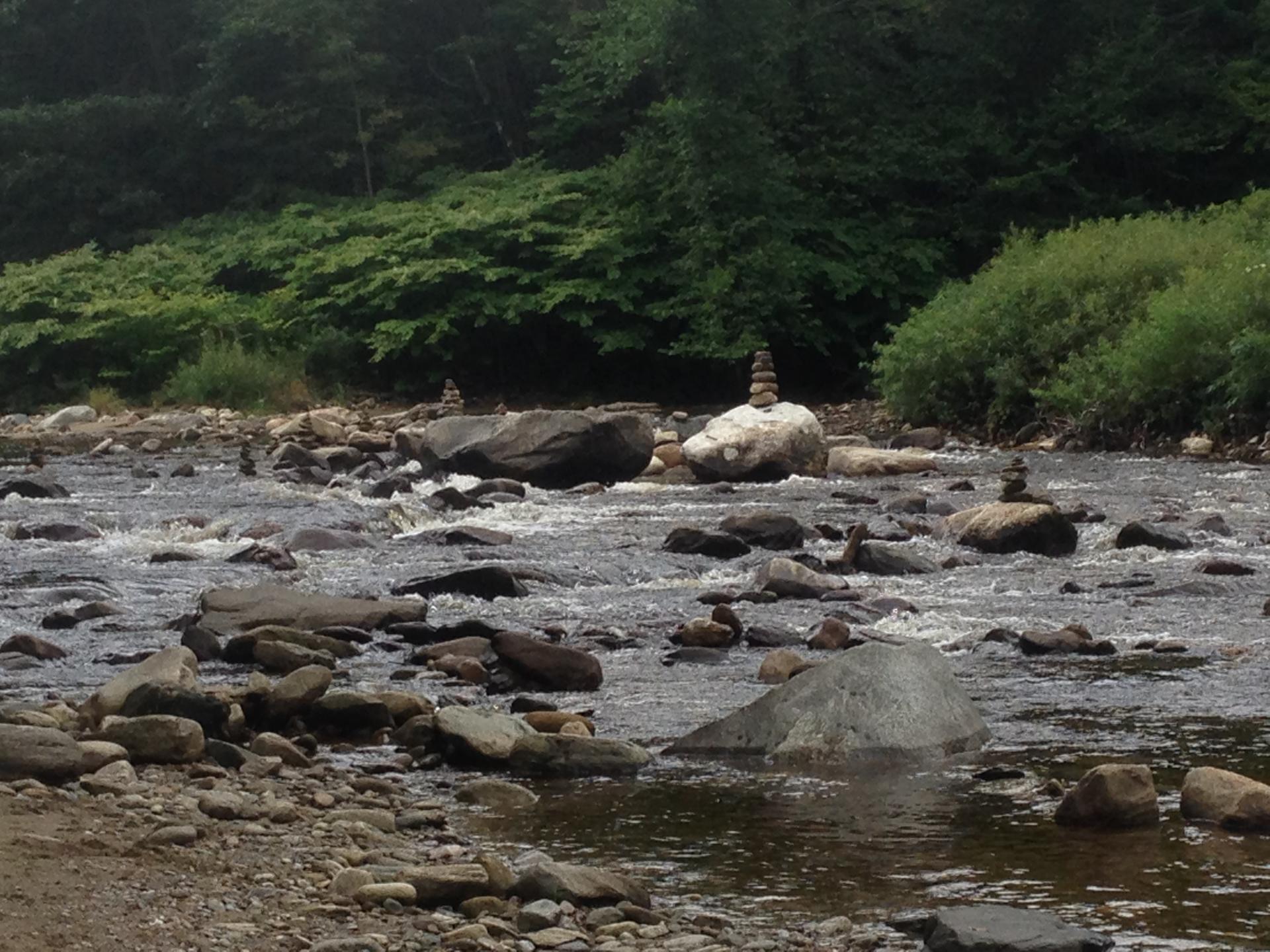 Rocky river with stacked stones on banks and in water, under diffused light.