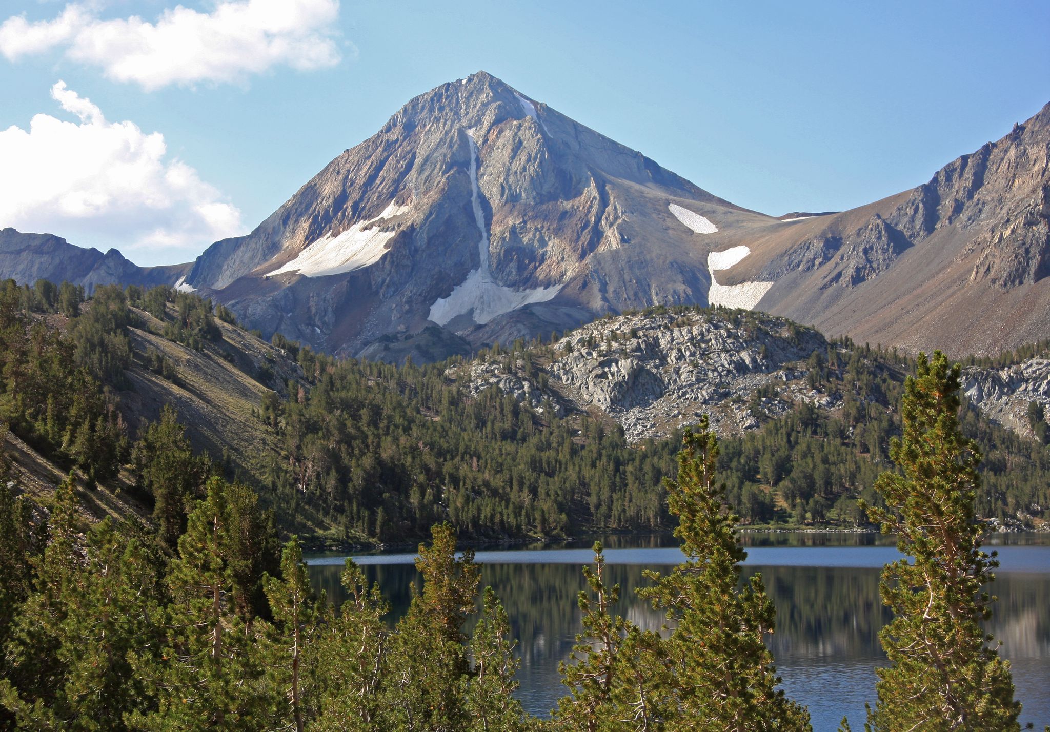 Snow-capped mountain overlooking a lake and dense pine forest, clear sky. - Convict Creek Trail