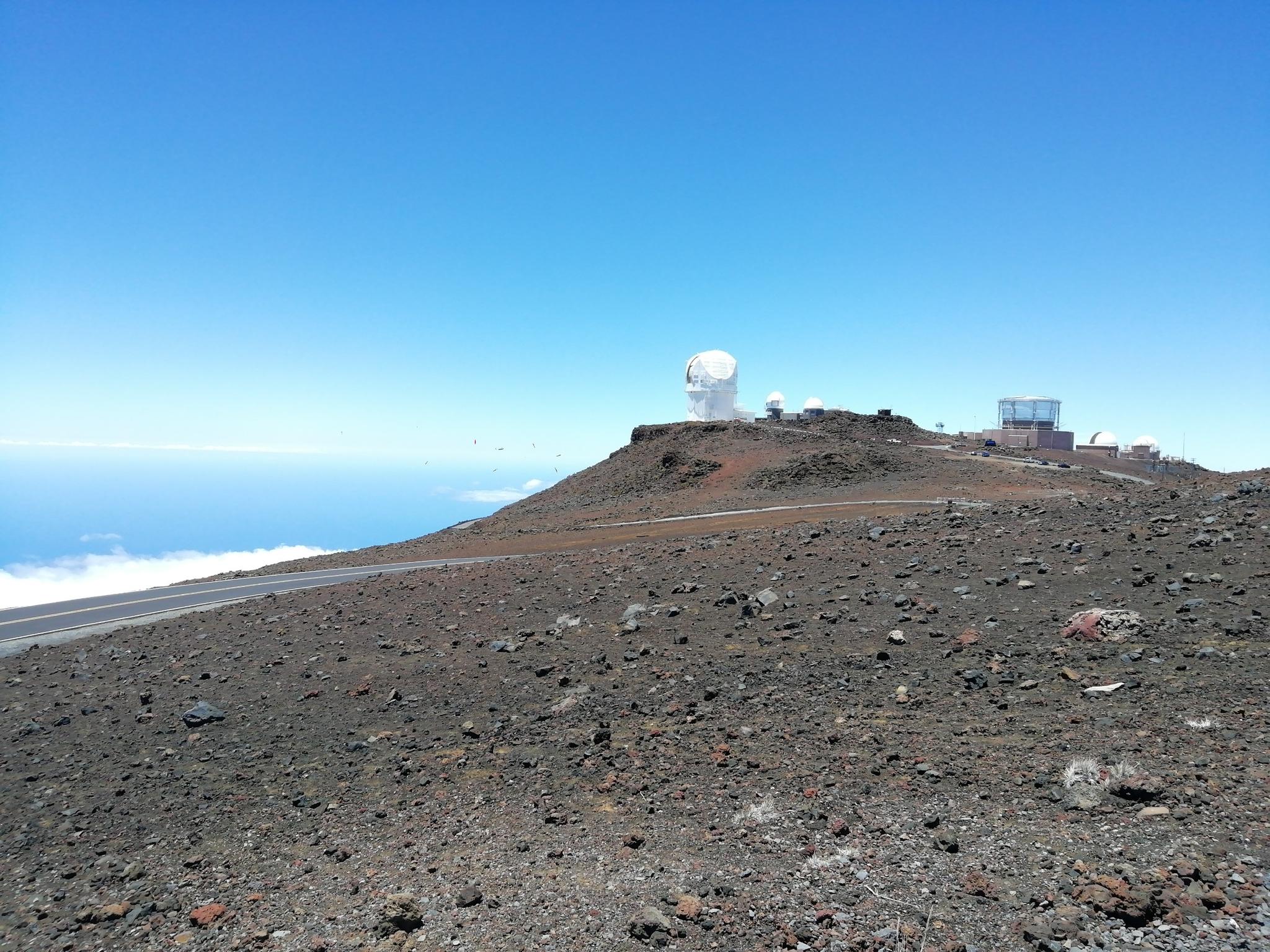 Distant white observatory domes on a rocky hill above clouds under a clear sky.