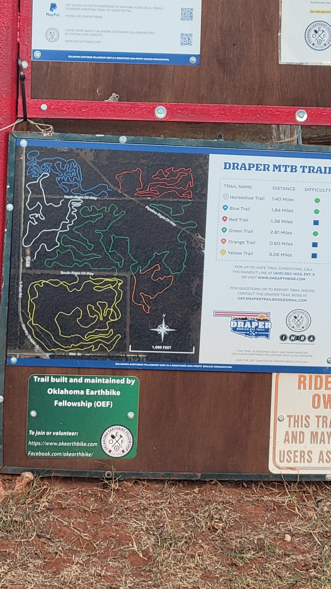 A weathered outdoor information board displays a detailed trail map and text under daylight.