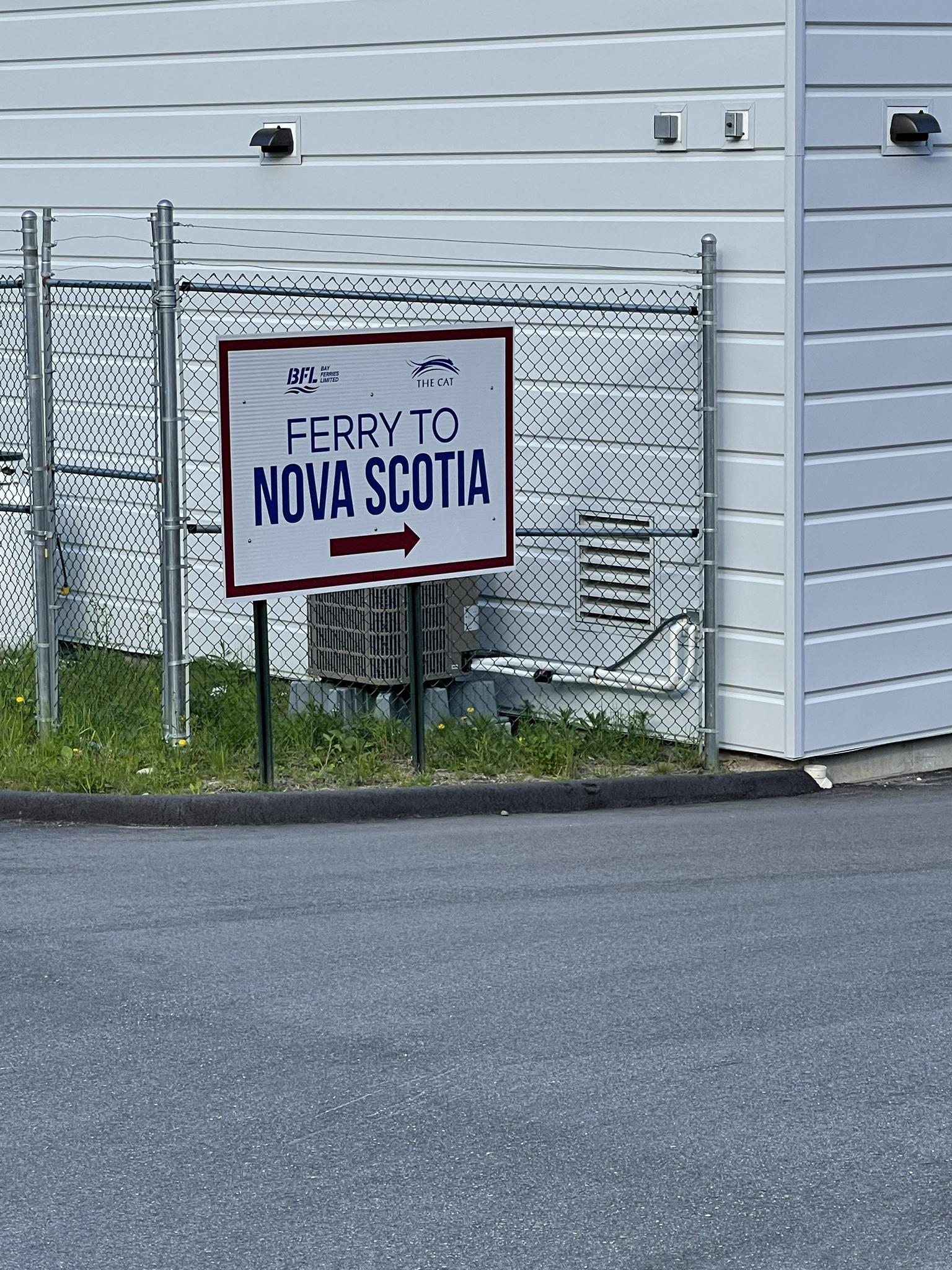 A white sign on a chain-link fence next to a building.