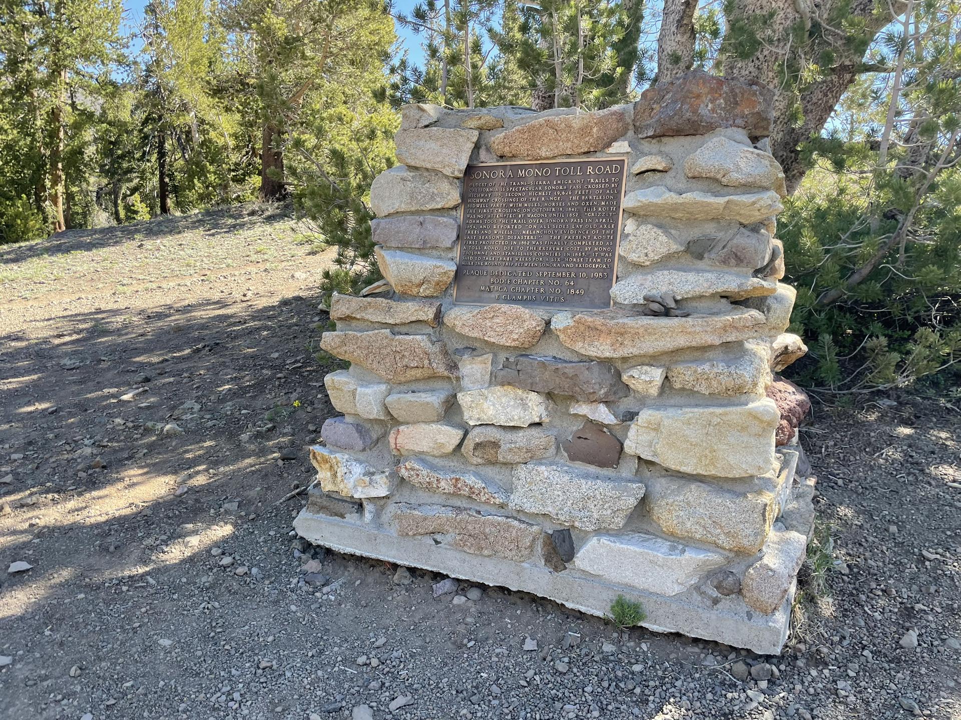 A stone monument with a plaque stands on a dirt path near trees.