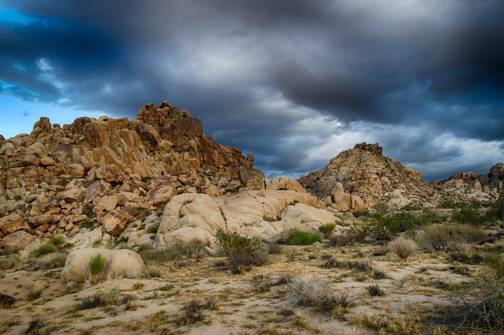 Dramatic desert landscape with large rock formations under dark, stormy clouds.