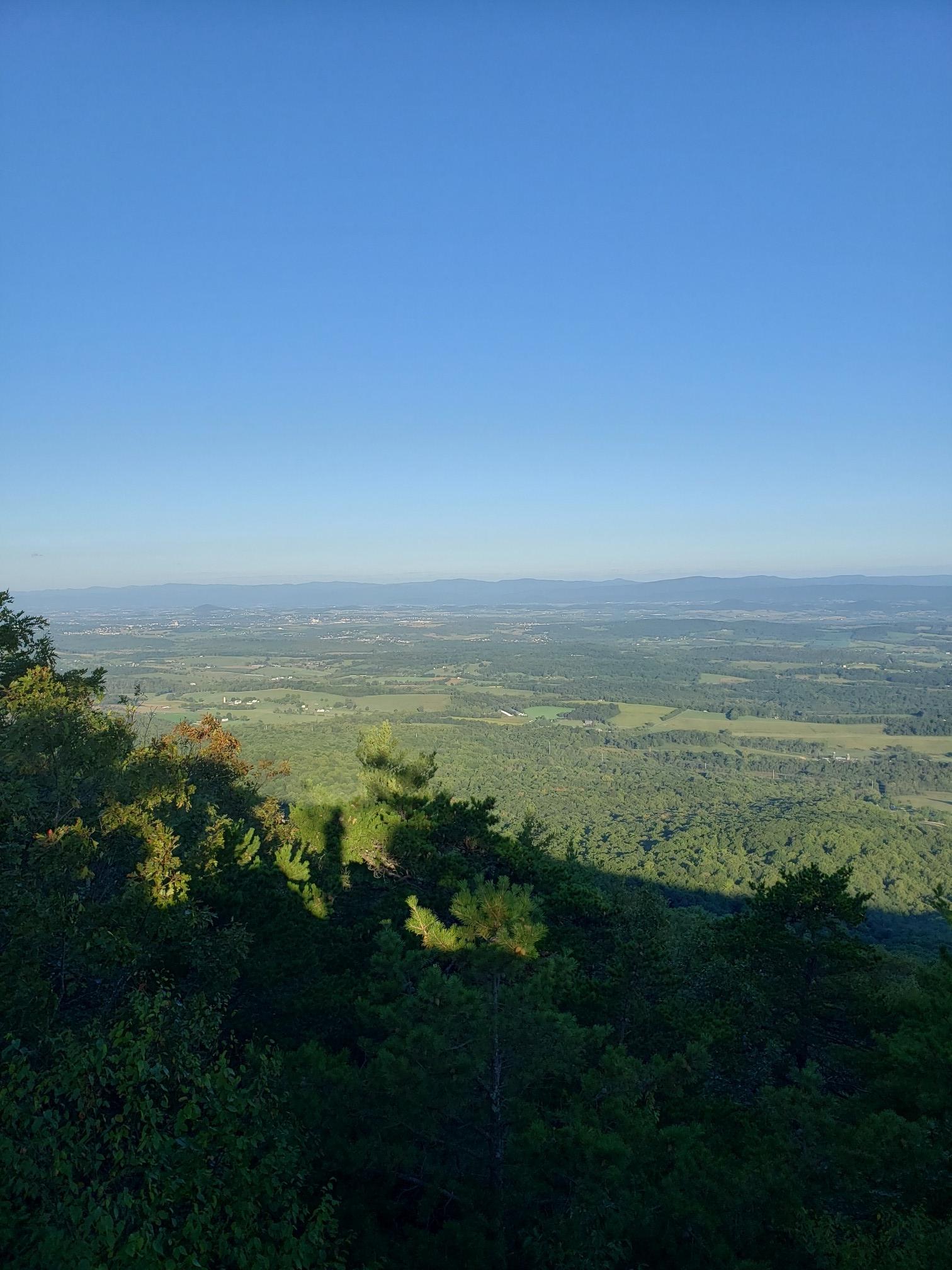 Panoramic view of a green valley and distant hills under a bright blue sky.