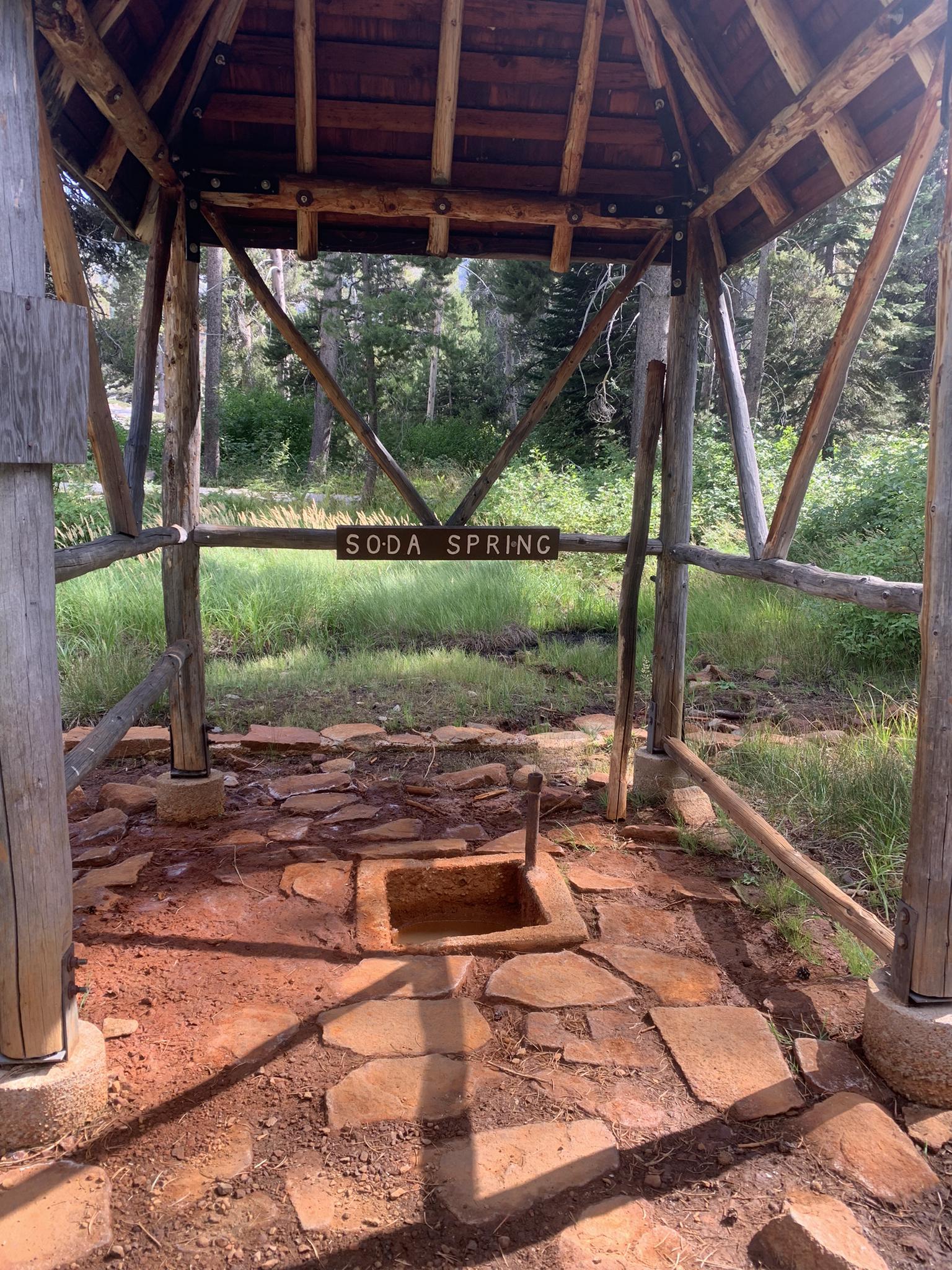 A rustic wooden shelter over a natural spring with a "Soda Spring" sign.