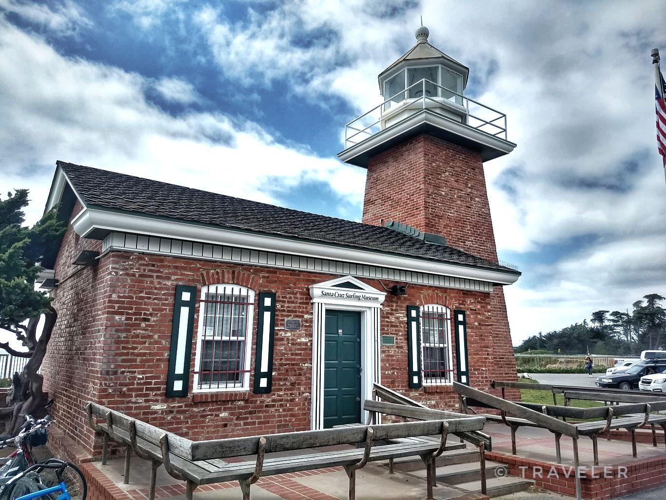 Red brick lighthouse building with a tower under a cloudy sky.