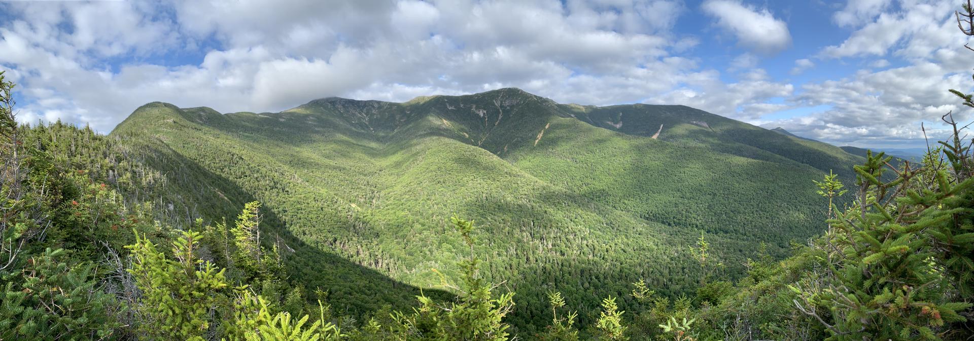 Panoramic view of lush green mountains under a partly cloudy sky.