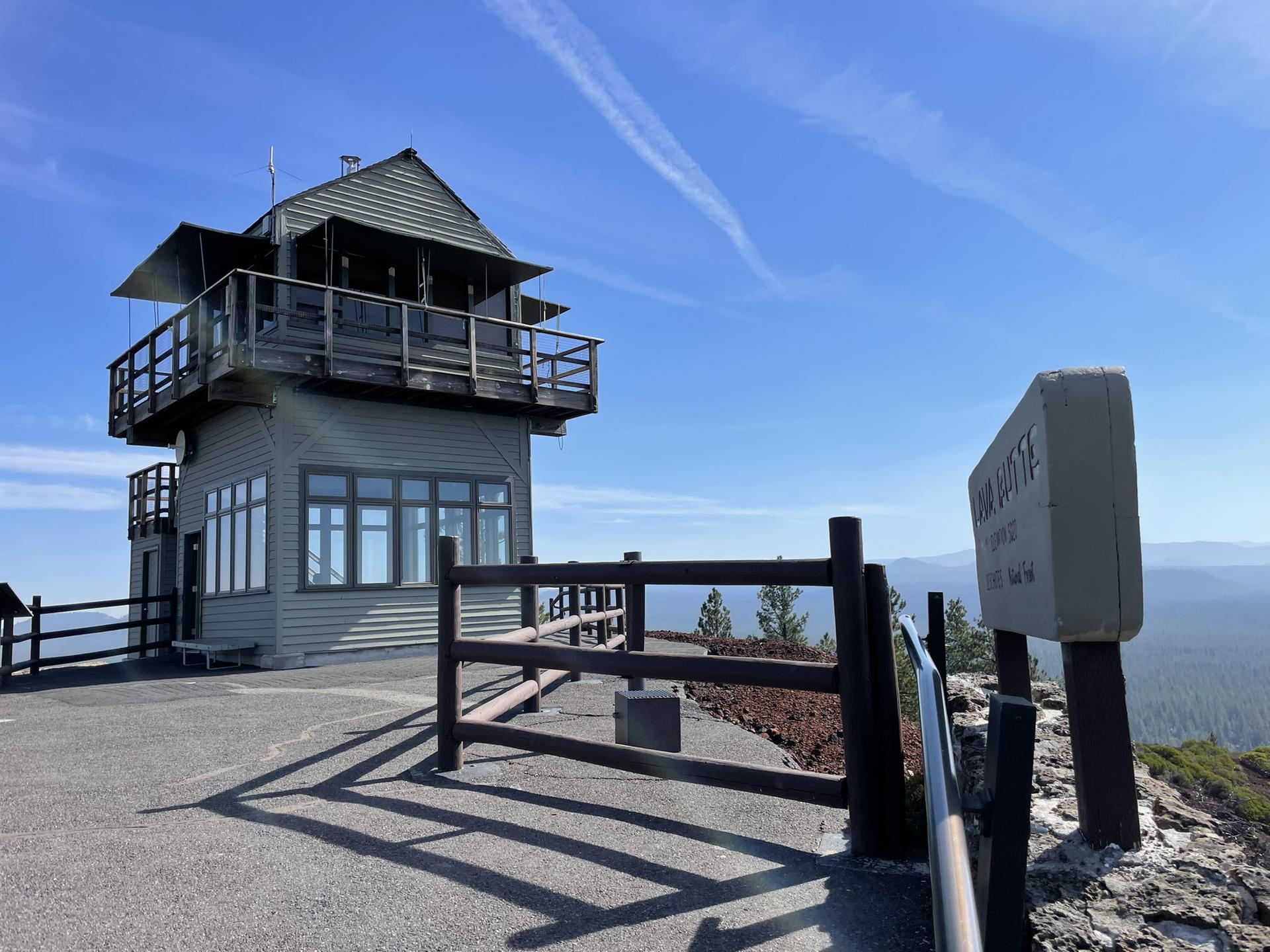 A multi-story lookout tower on a hill, with a fence and distant landscape.