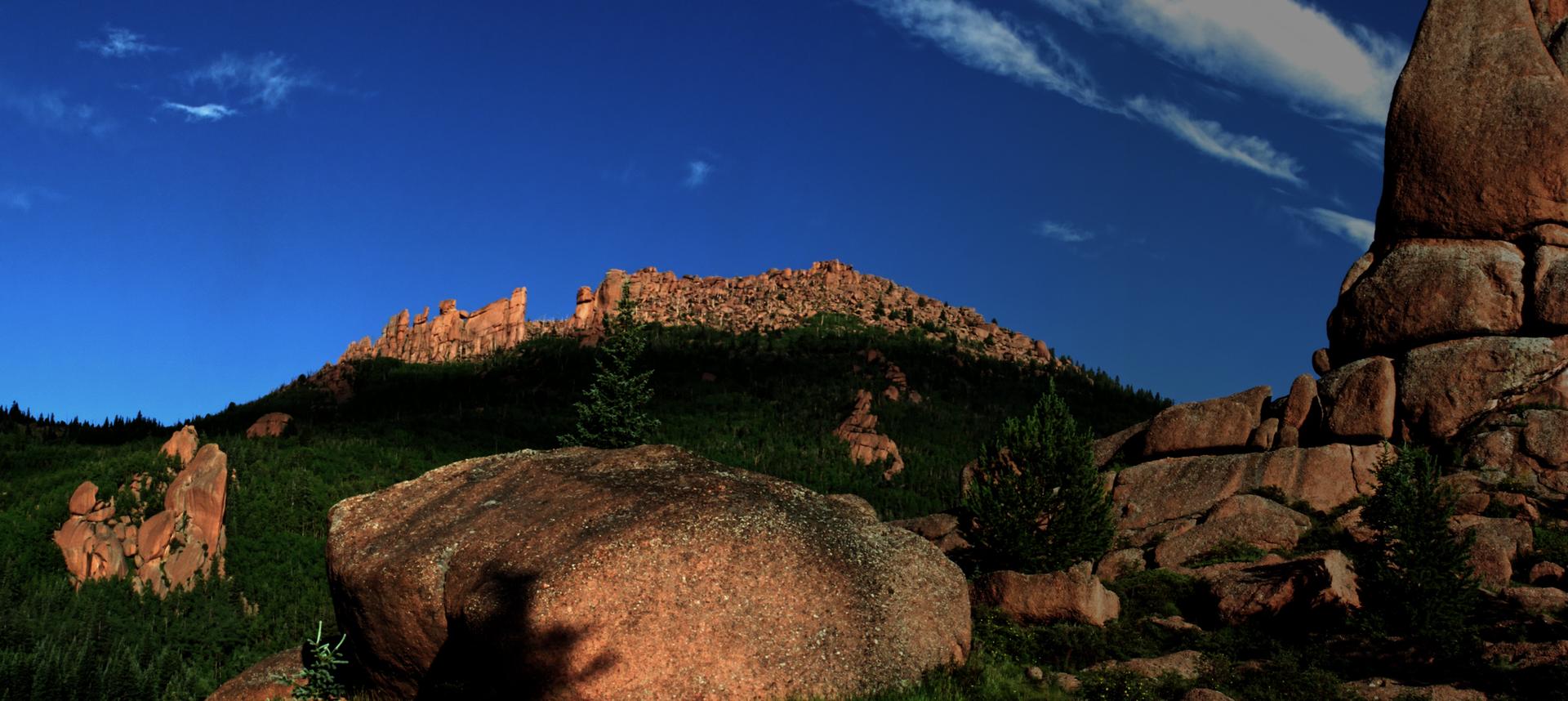 Panoramic view of sunlit rock formations and green hills under a clear blue sky.