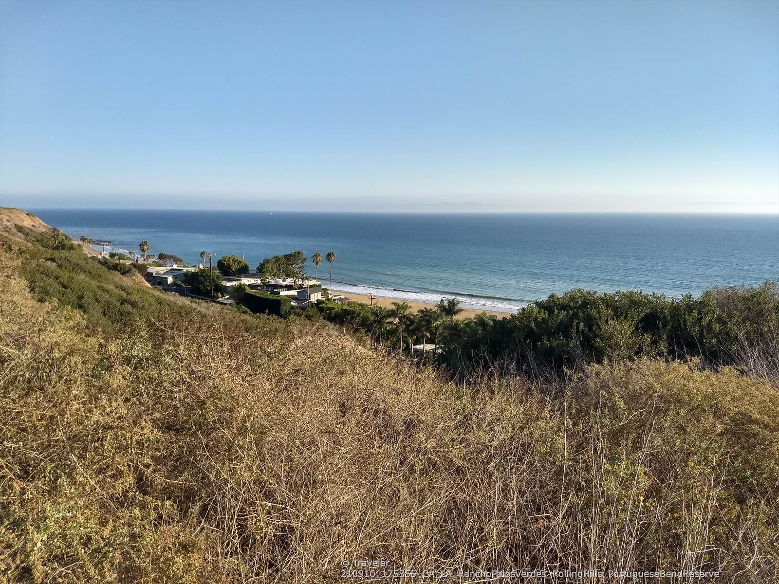 Dry grassy hillside overlooking a sunny beach, calm ocean, and distant houses. - Palos Verdes Drive Loop