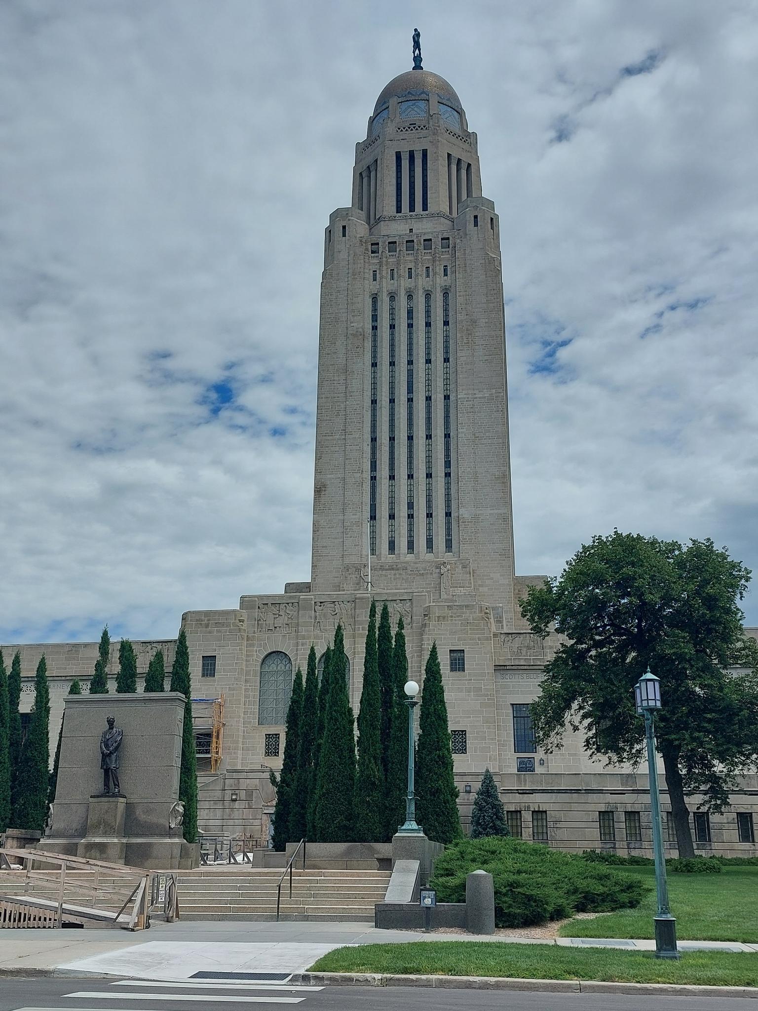 Tall stone building with a dome and statue under a cloudy sky.