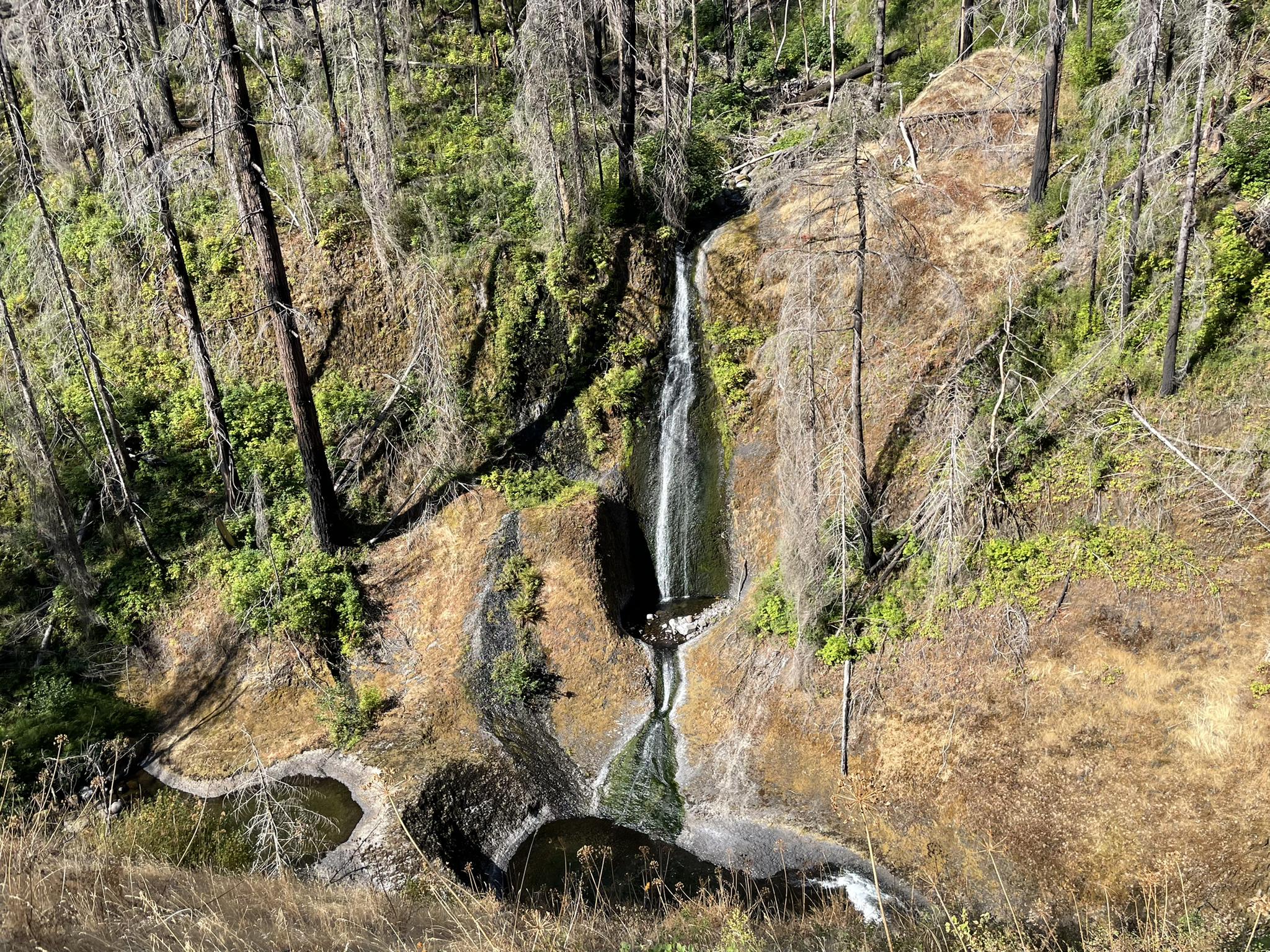 A waterfall cascades down a multi-tiered rock face in a forest.