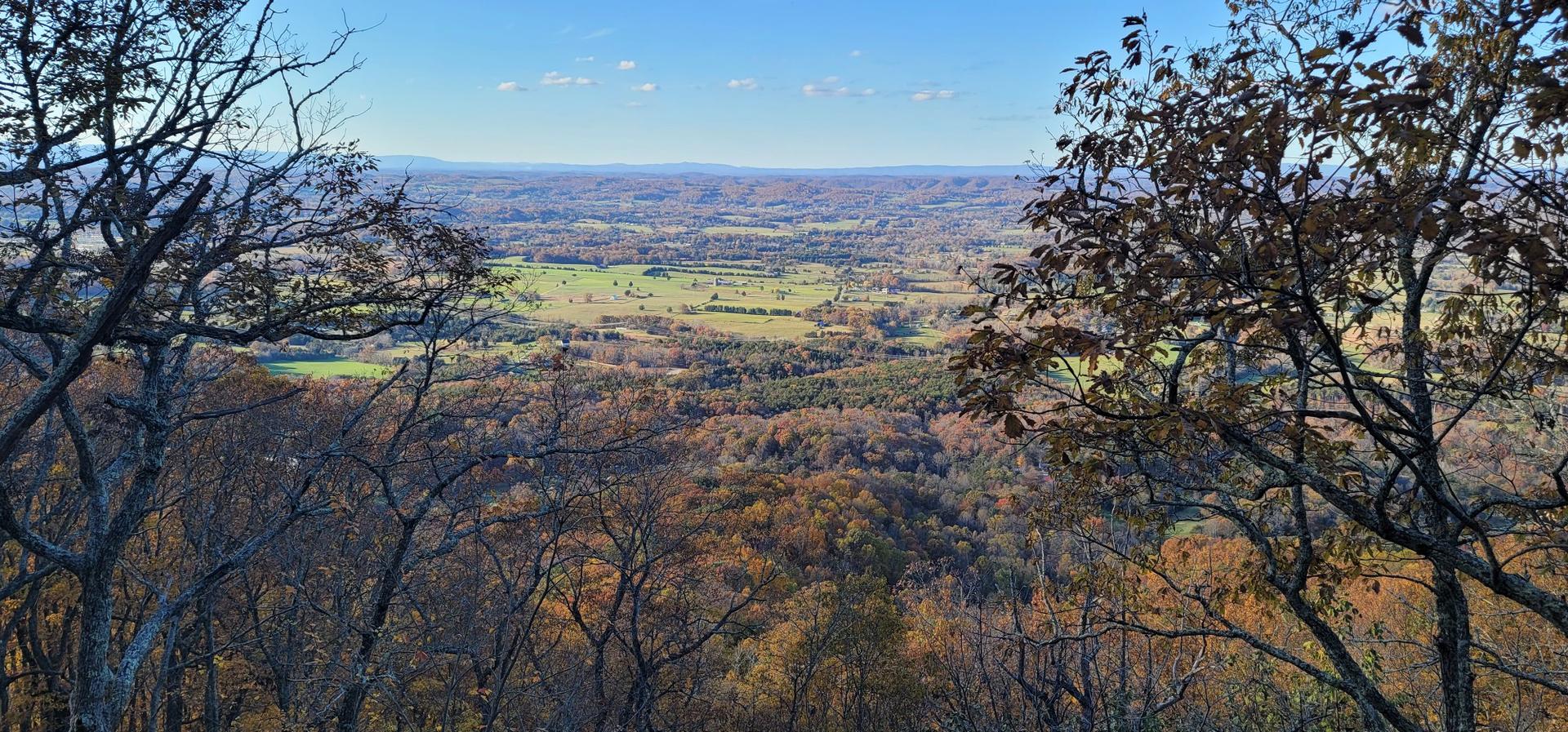 Wide view of a valley with fields and autumn trees under a blue sky.