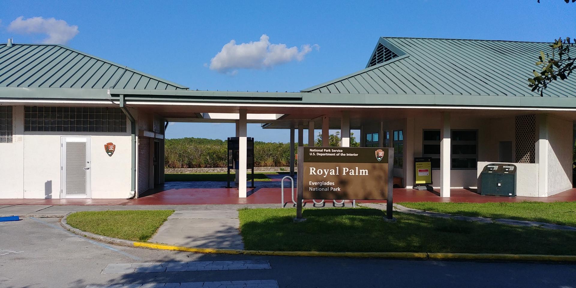 Building entrance with a sign, bright sun, and blue sky.