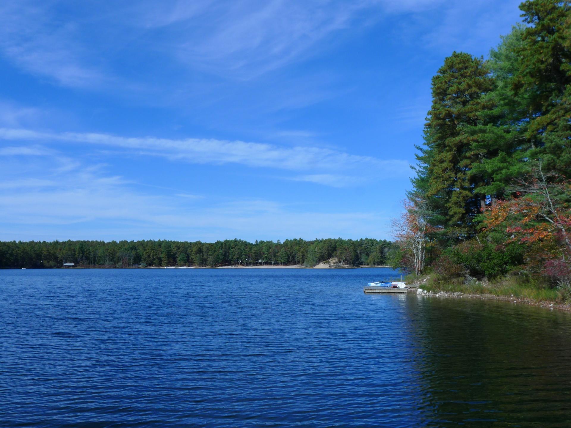 Blue lake with forested shores under a clear sky, small dock visible.