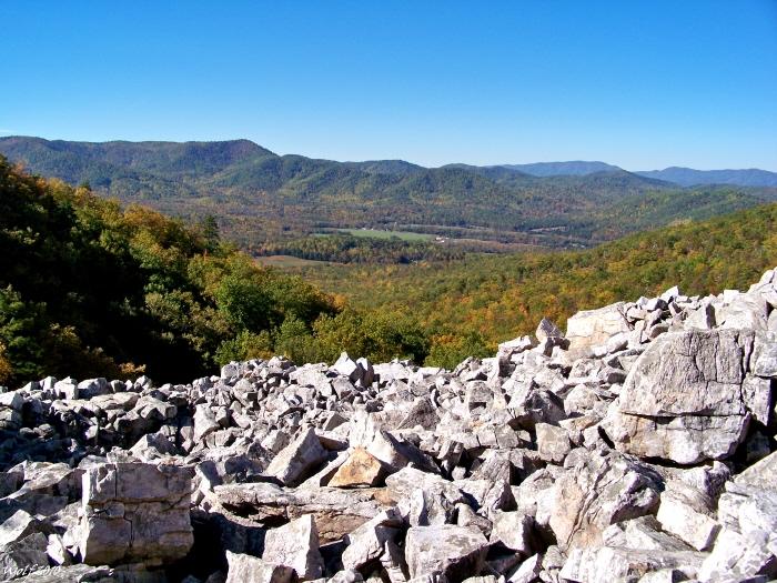 Bright, sunny view over a rocky slope to forested mountains and a valley.