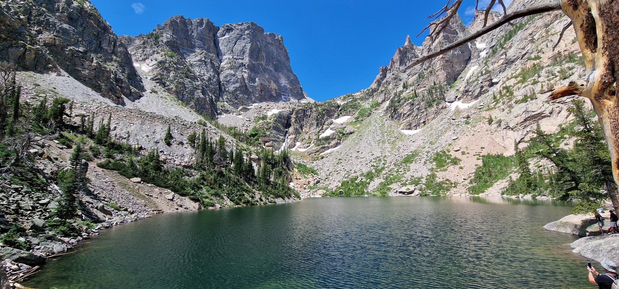 Serene mountain lake surrounded by towering rocky peaks under a bright blue sky.