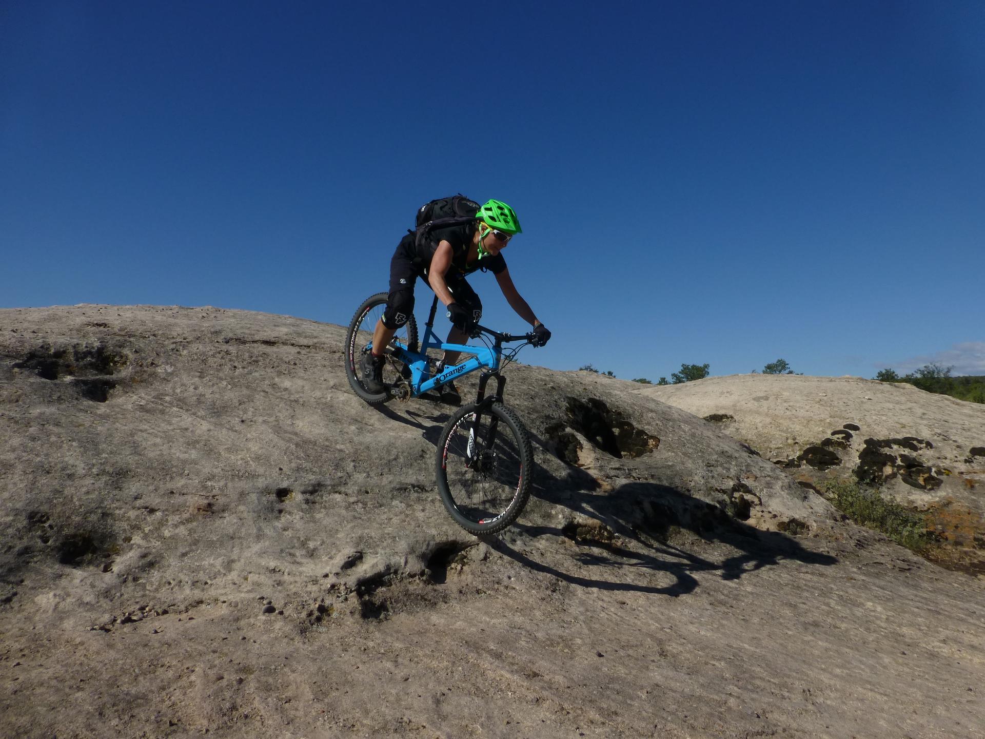 Person mountain biking up a large rock formation under a clear blue sky.