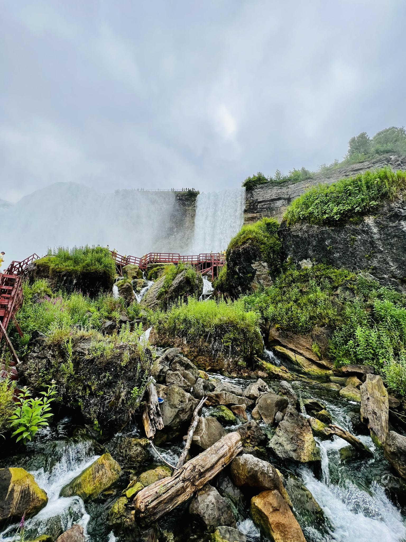 Waterfall cascading over rocks with red stairs and lush green foliage.