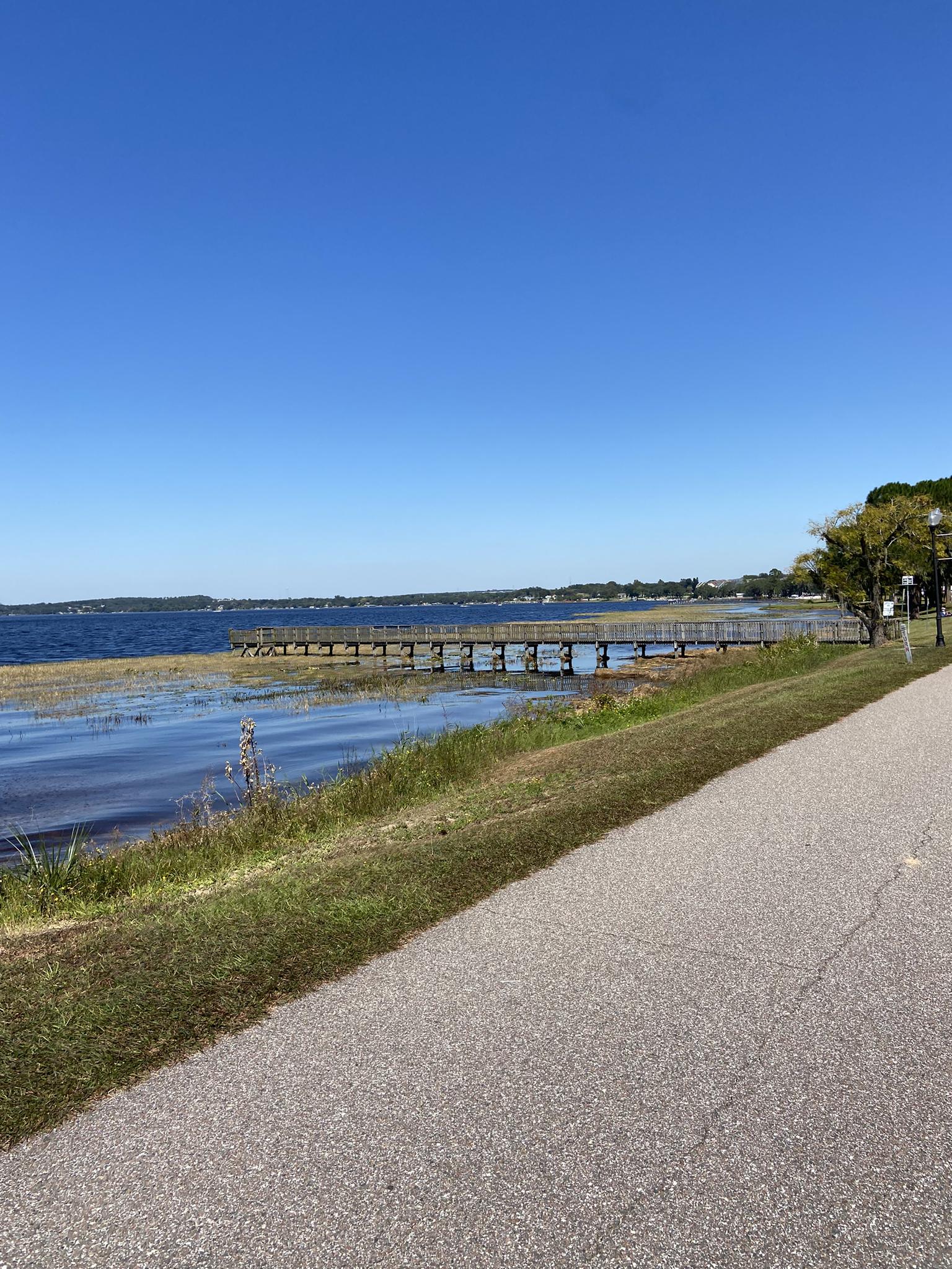 Sunny day with a paved path beside a lake and wooden boardwalk.