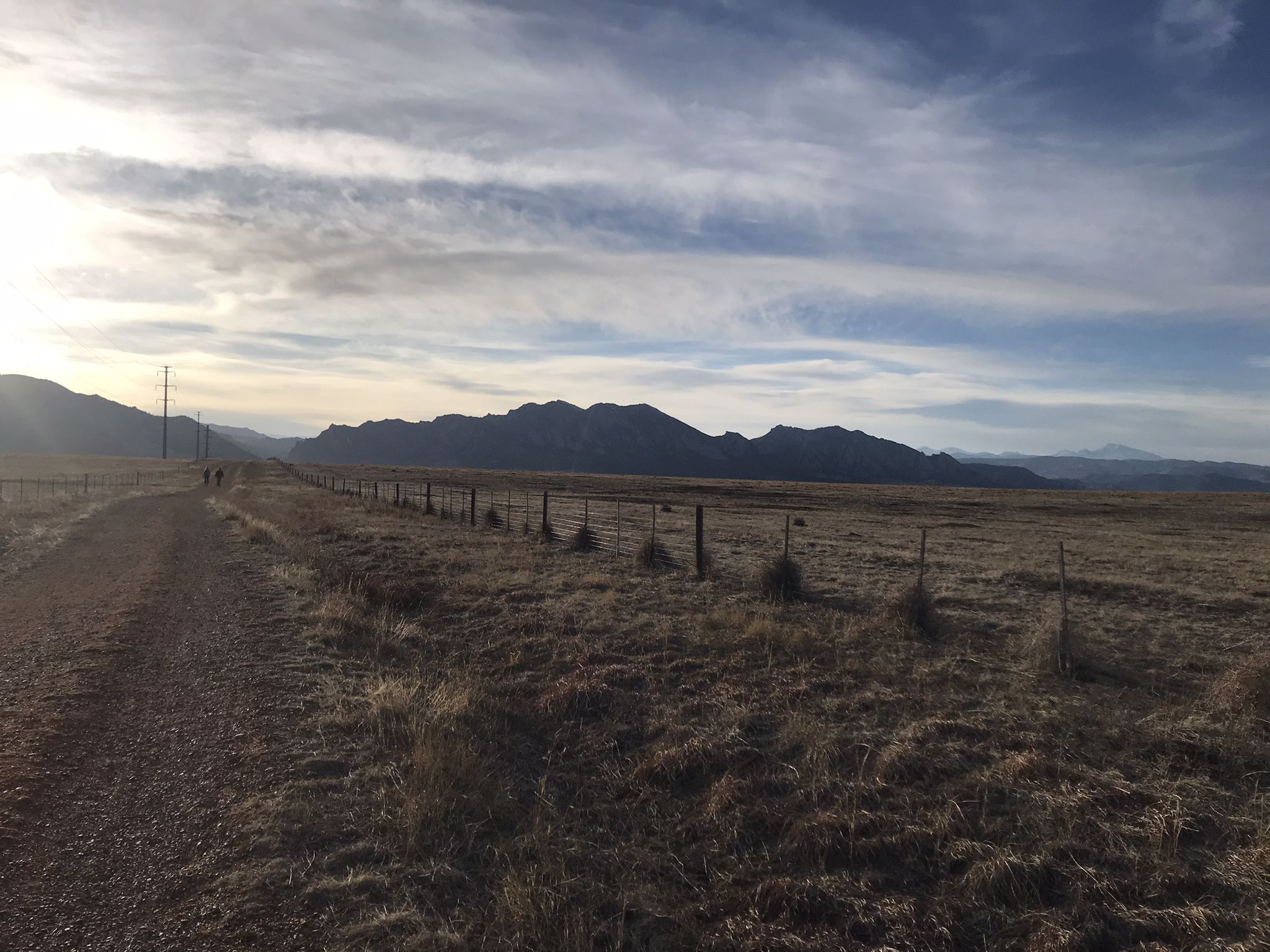 Dirt road beside a fence, leading towards distant mountains under a cloudy sky. - Marshall Mesa Loop