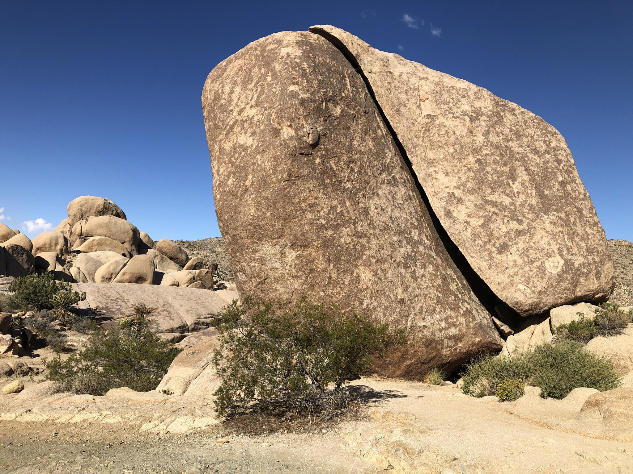 A massive split boulder stands prominently in a desert landscape under a clear blue sky.