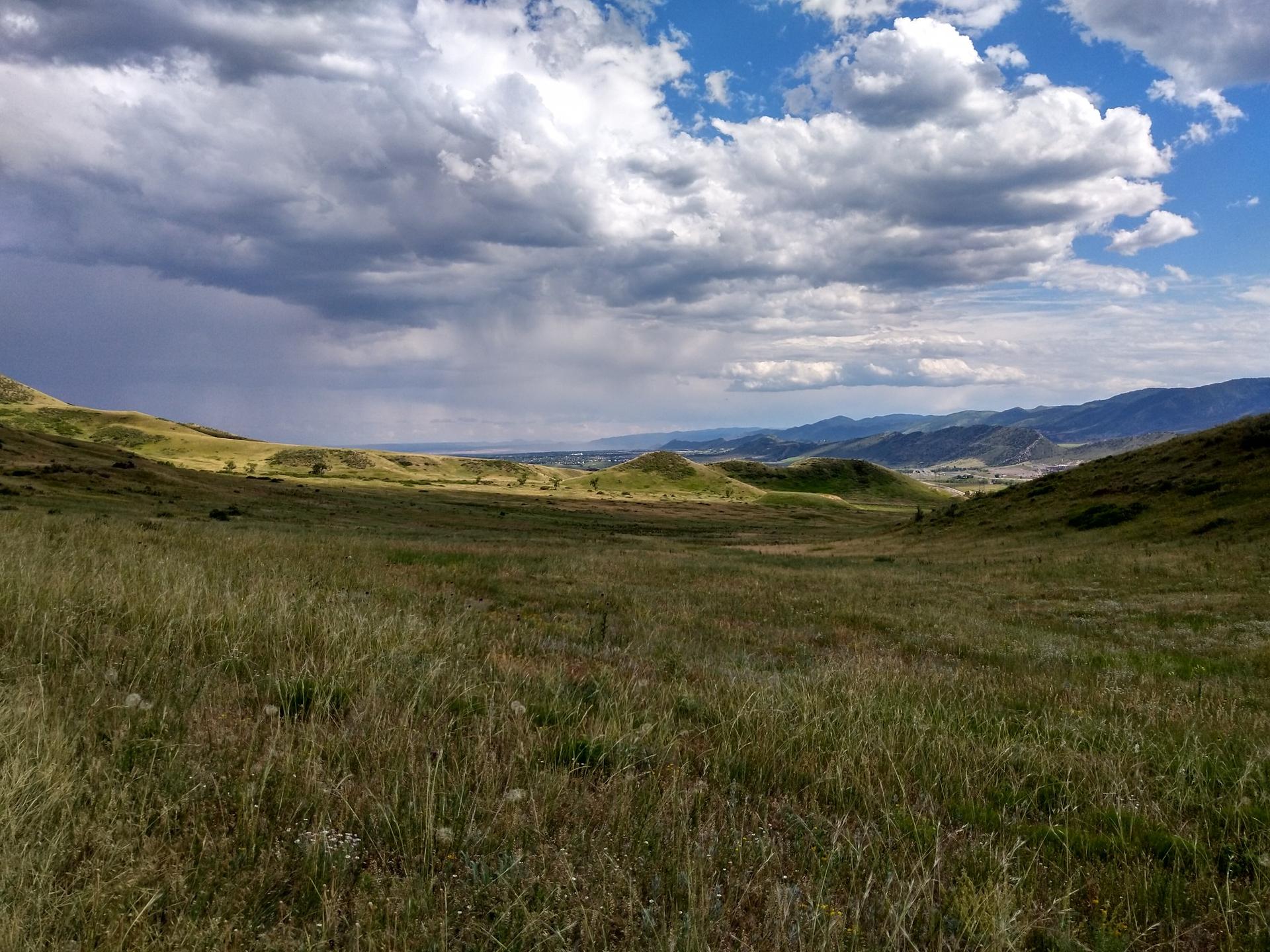 Expansive green valley with distant mountains under a dramatic cloudy sky.