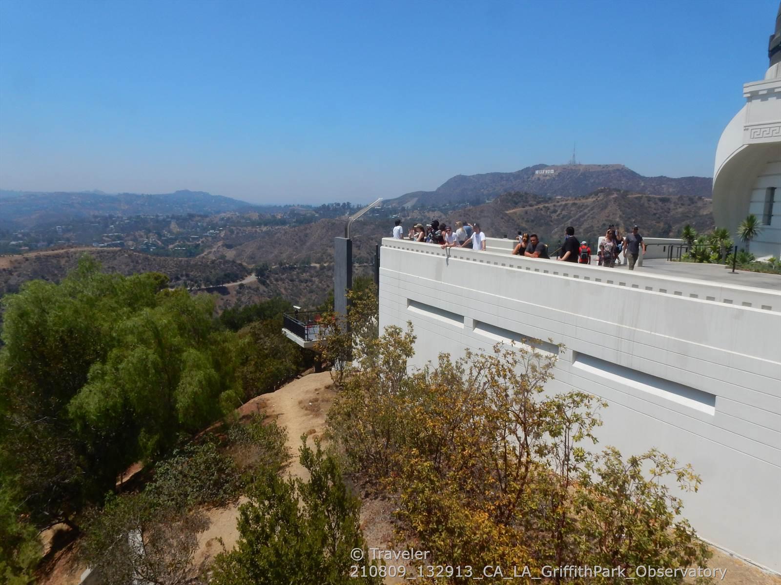 People on a white observation deck overlooking distant green hills and city.
