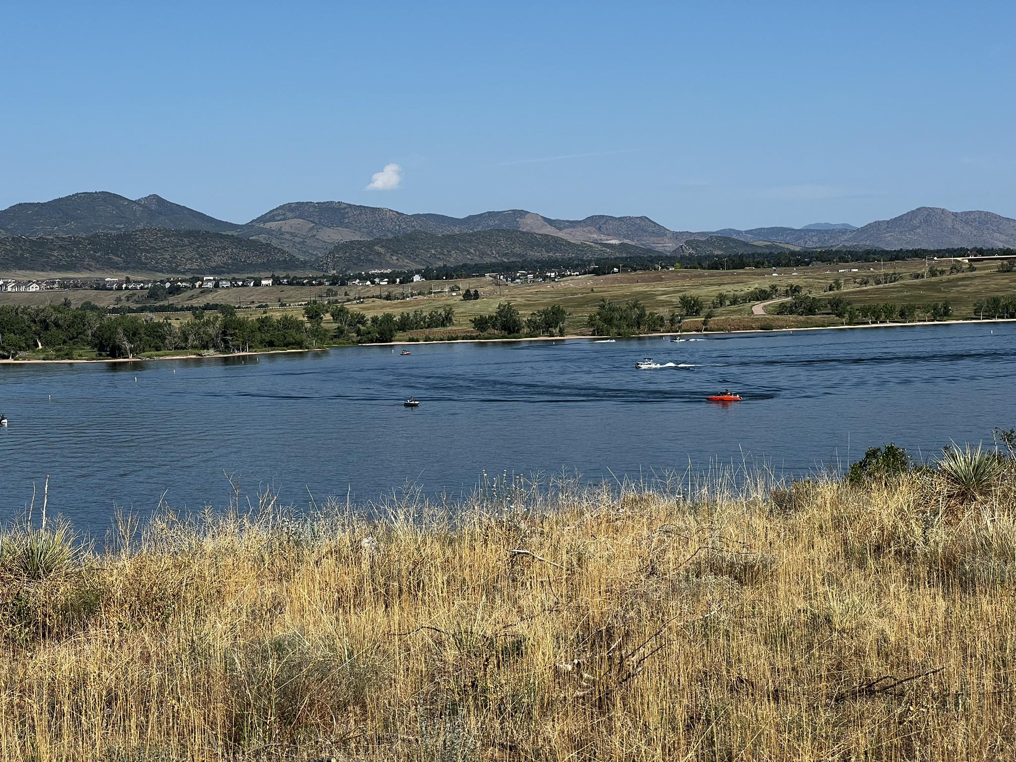 A large lake with distant mountains, boats, and dry grassy foreground.