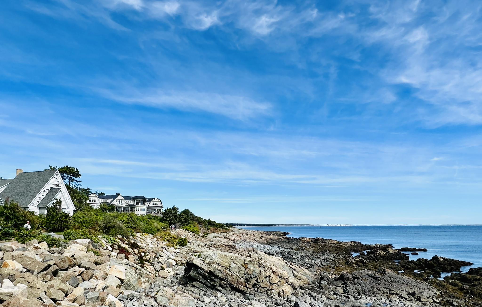 Rocky coastline with houses on a hill under a bright blue sky.