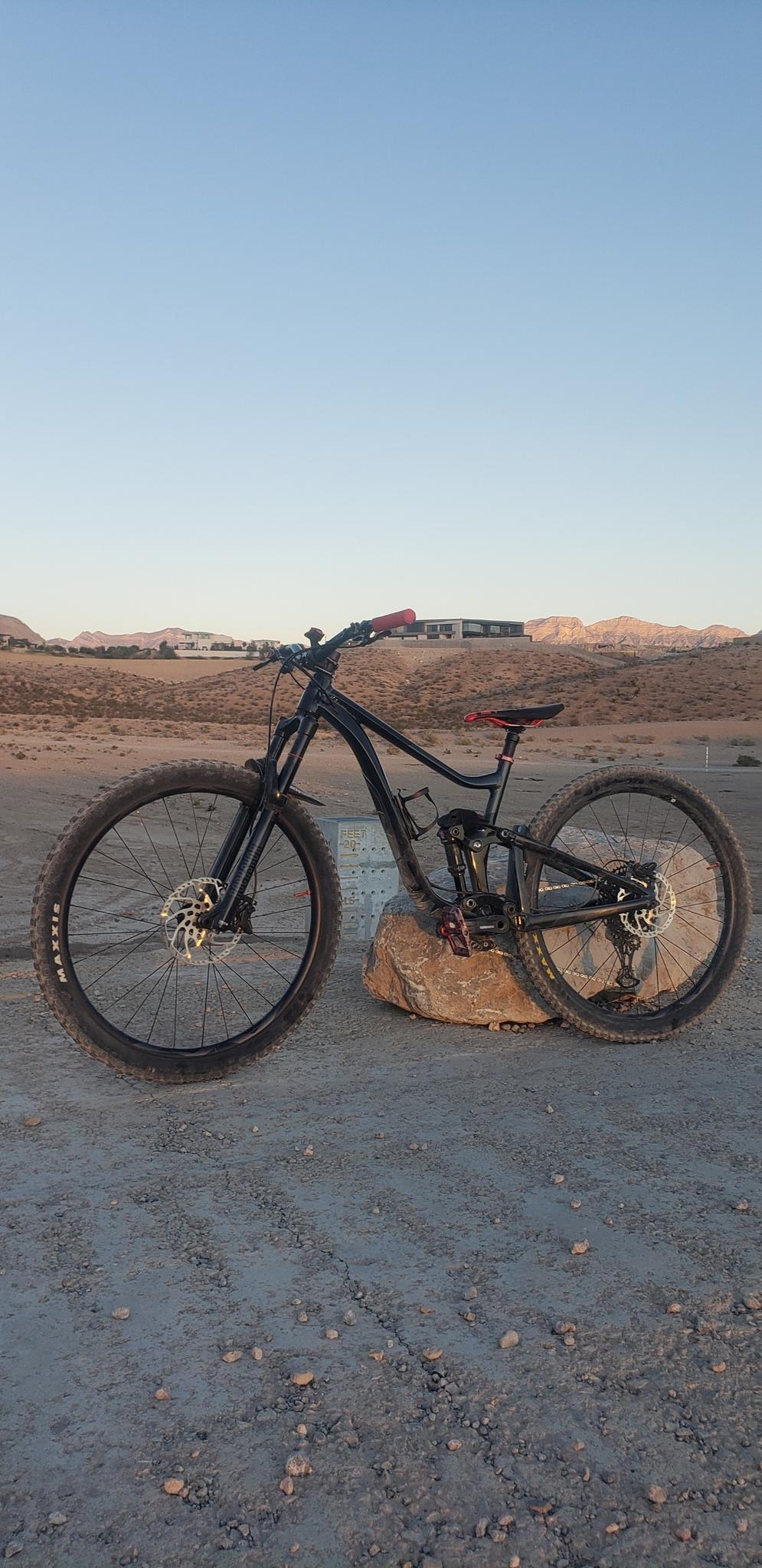 A black mountain bike stands on a rock in a desert landscape at dusk.