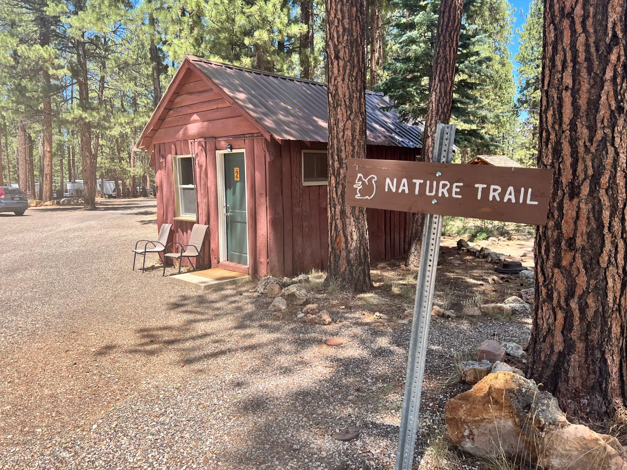 Red cabin and 'Nature Trail' sign in a sunny, forested area with gravel.