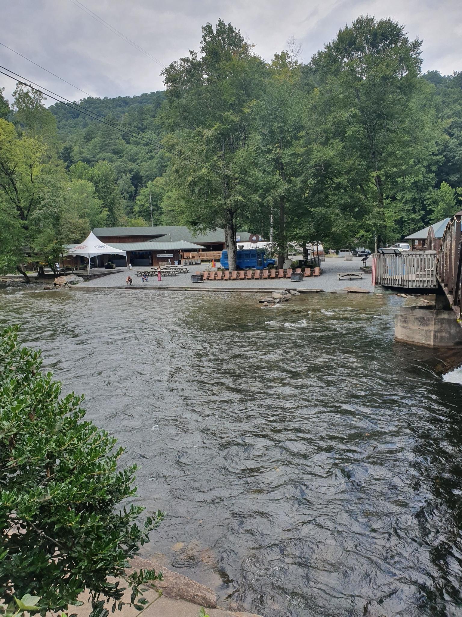 A wide river flows past buildings and green trees under an overcast sky.