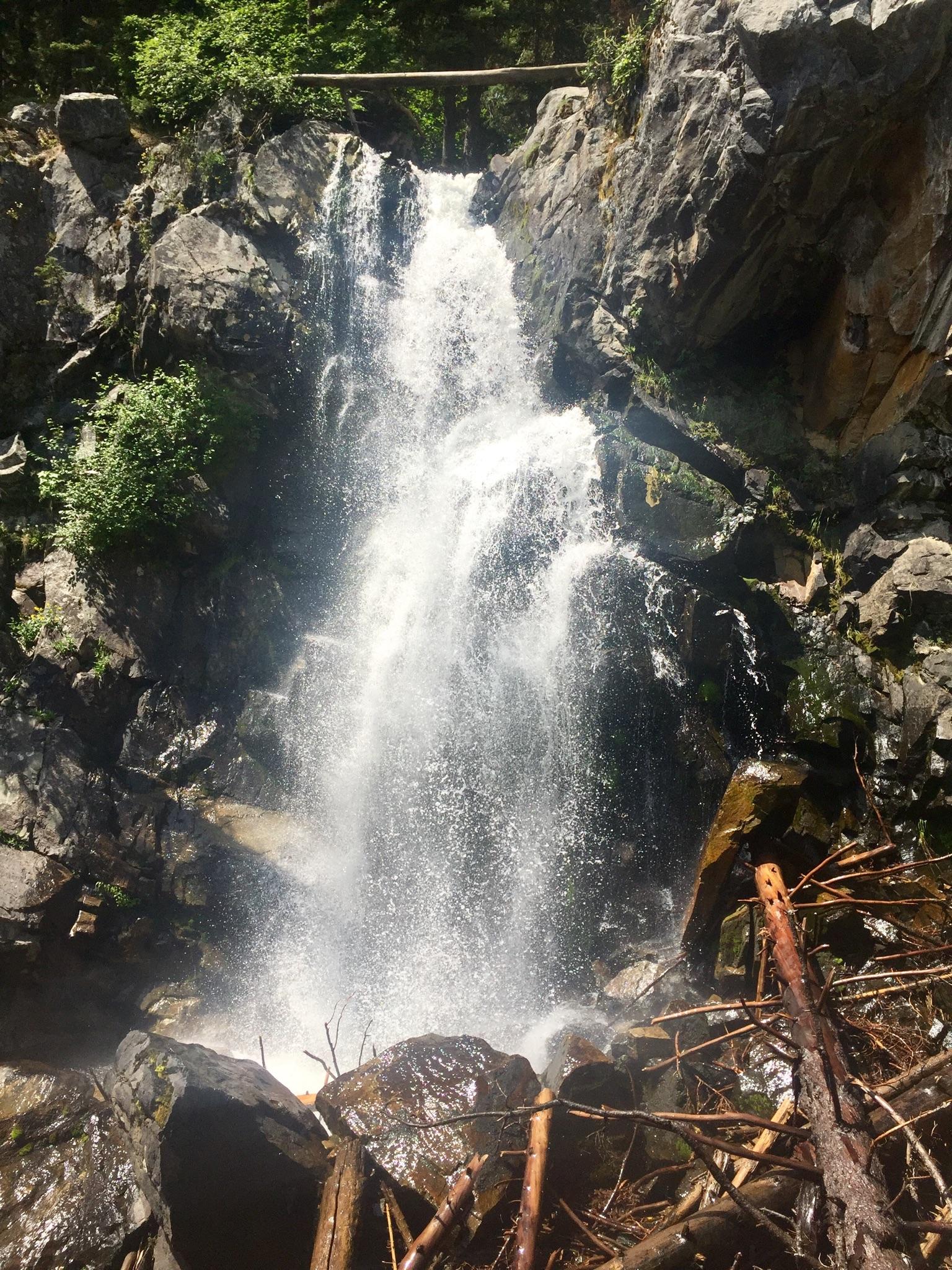 A powerful waterfall cascades down a rocky cliff surrounded by green foliage.