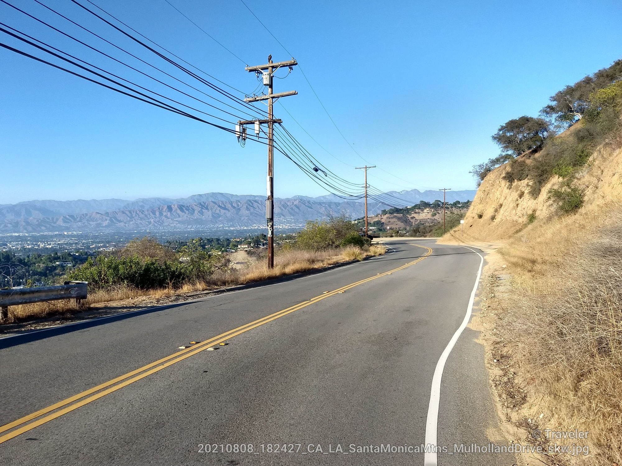 Winding road with power lines, dry hills, and distant city under clear sky. - Mulholland Drive Loop