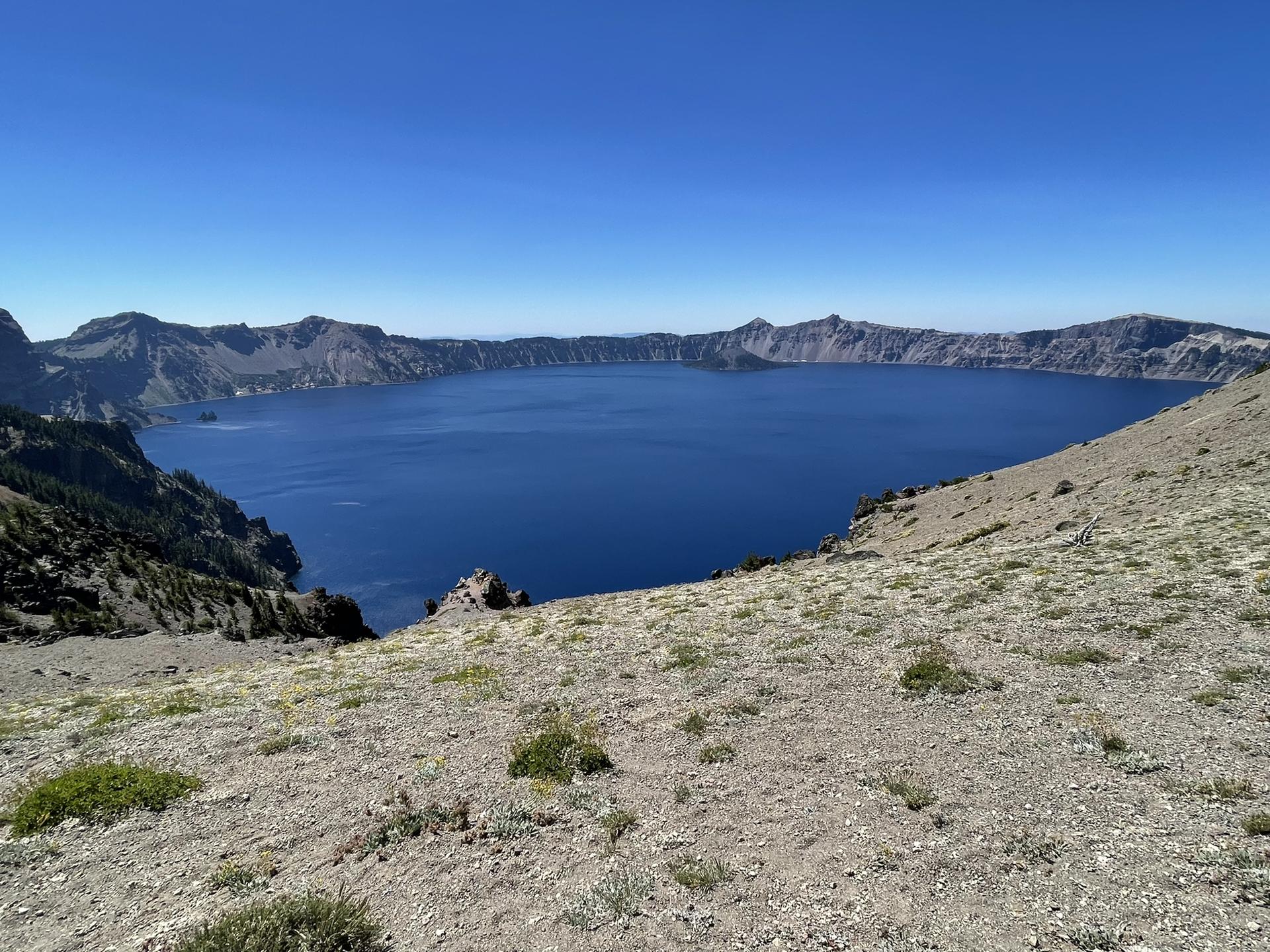 Wide view of a deep blue lake encircled by rugged, treeless slopes under a clear sky.