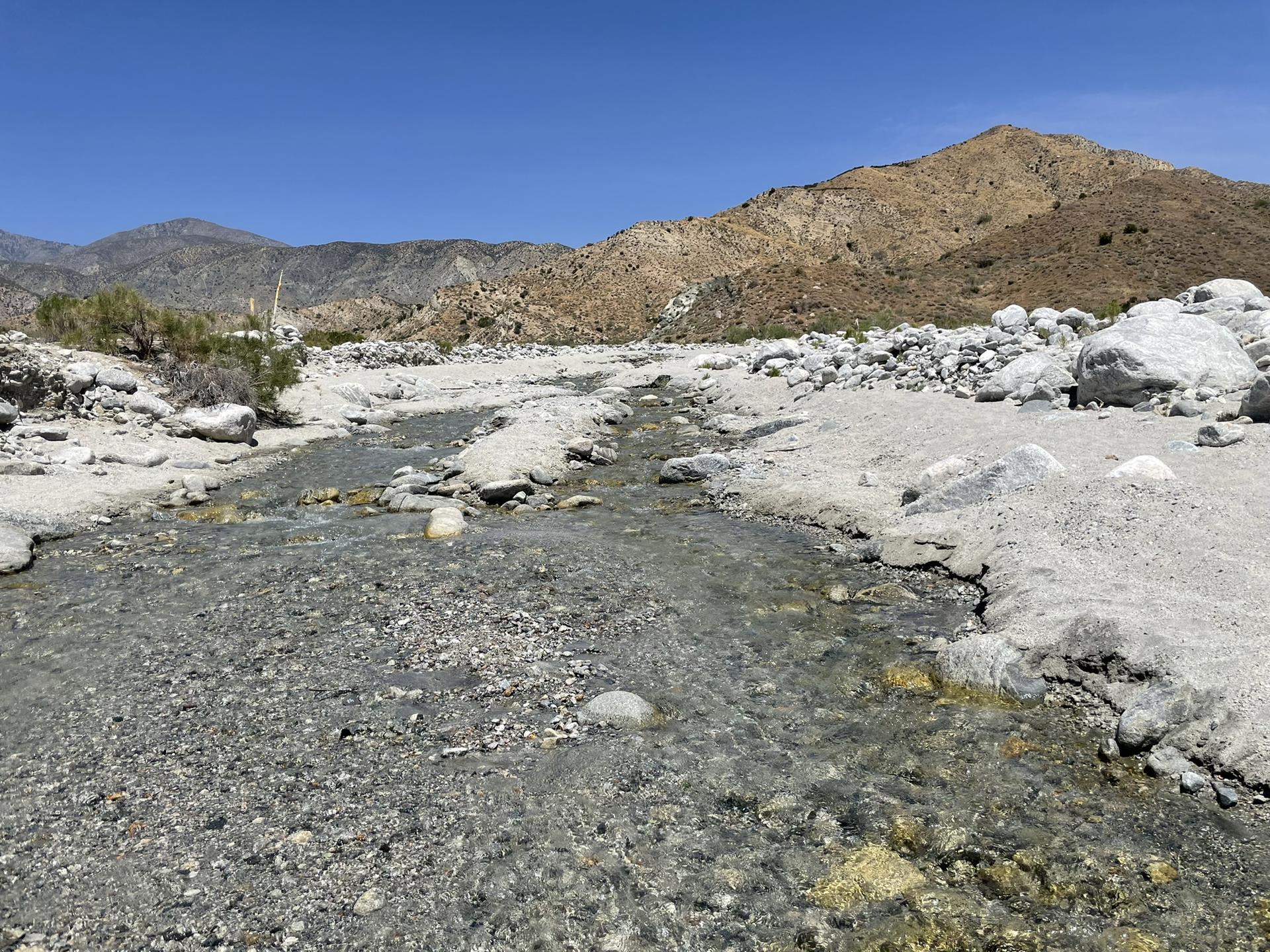 A shallow stream flowing over rocks in a desert landscape with mountains.