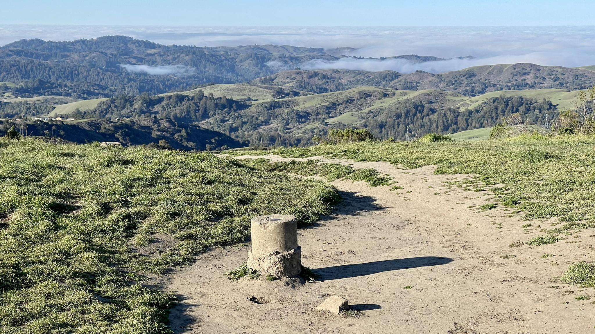 Concrete marker on a dirt path overlooking misty green hills.