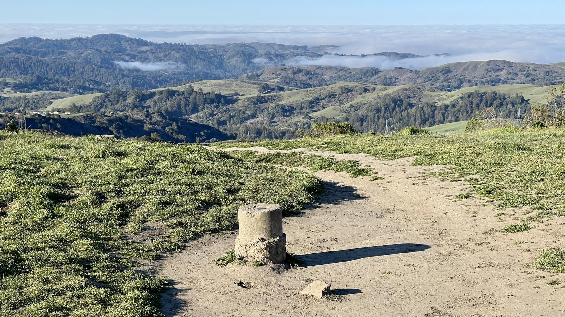 Concrete marker on a dirt path overlooking misty green hills.