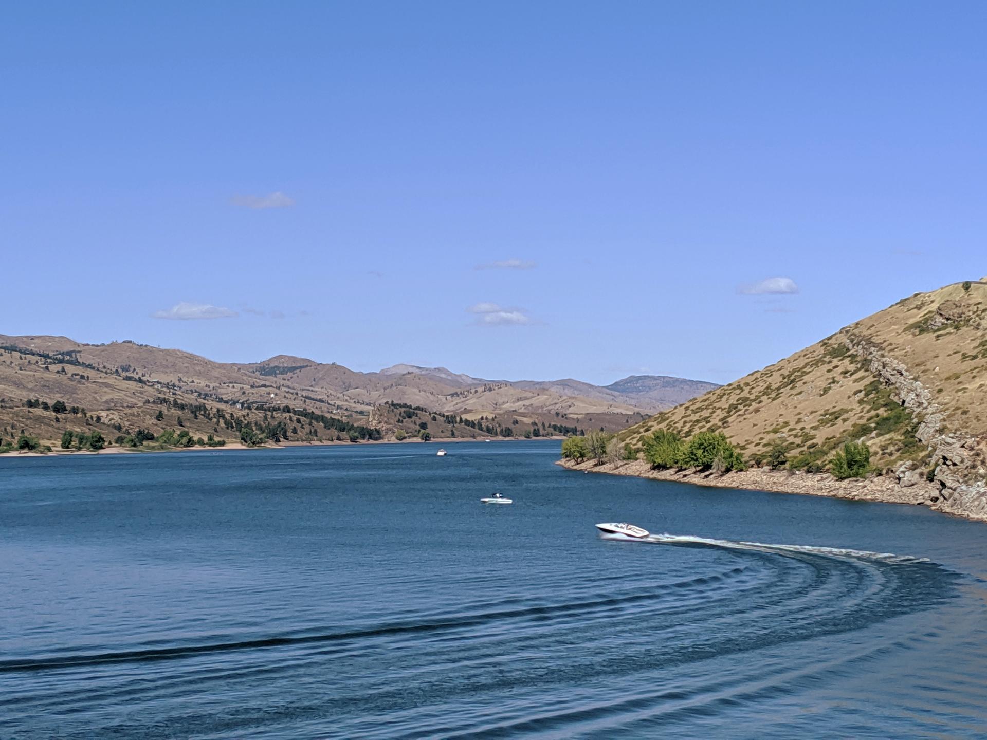 Wide lake with mountains, a speeding boat, and clear blue sky.