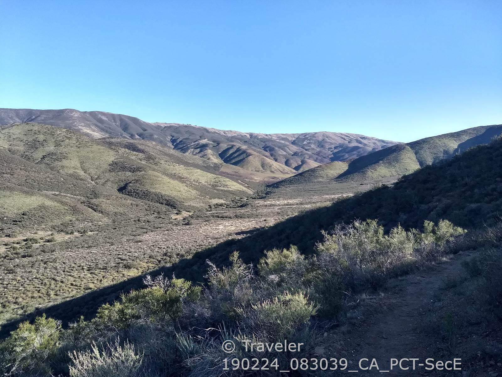 Expansive view of sunlit, rolling hills and valleys under a clear blue sky.