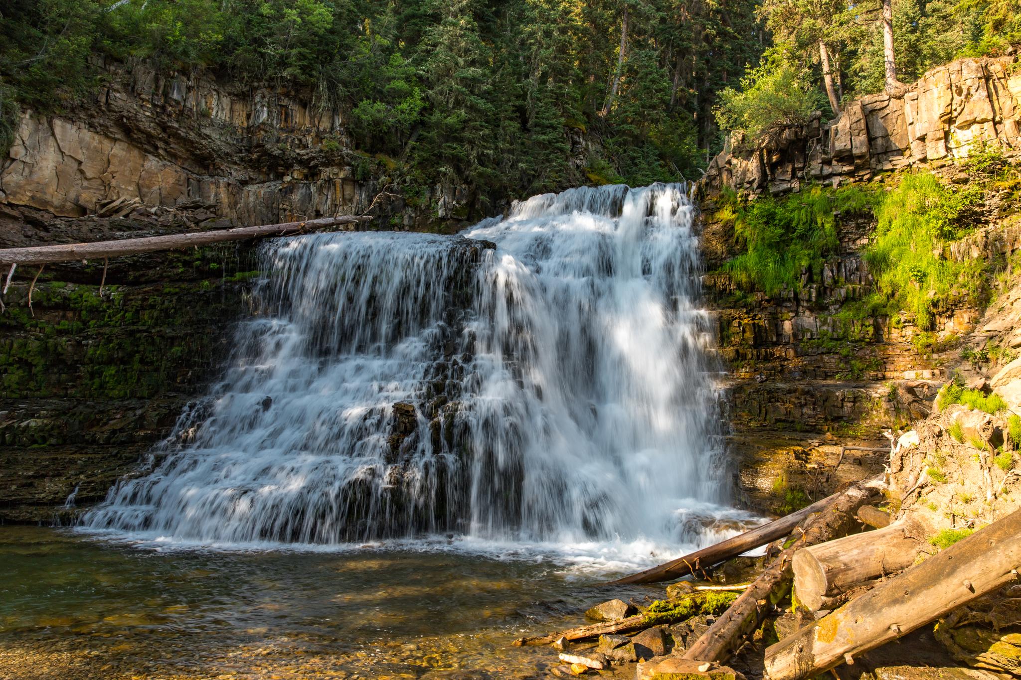 A wide, tiered waterfall cascades into a pool surrounded by lush forest.