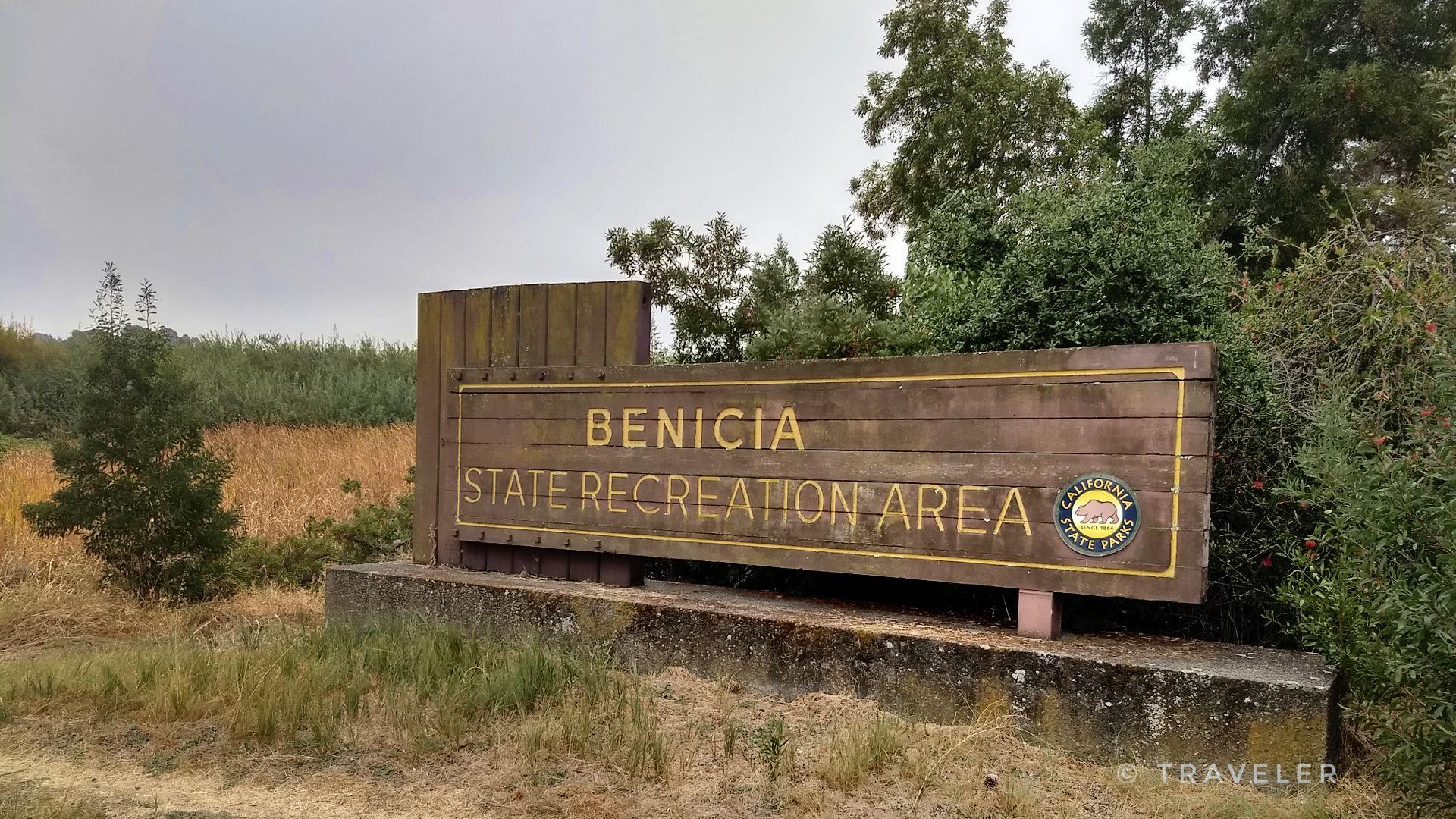 A large wooden sign stands among trees and dry grass on an overcast day.