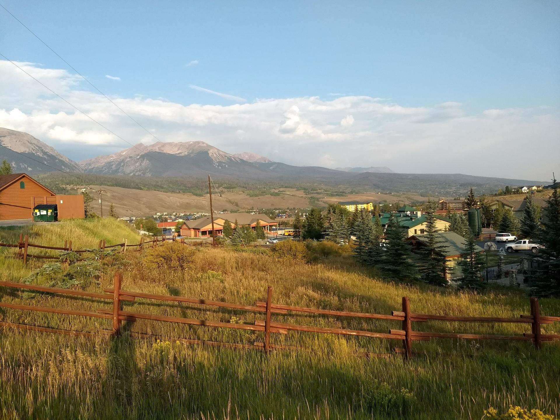 Sunny view of a mountain town with a wooden fence foreground.