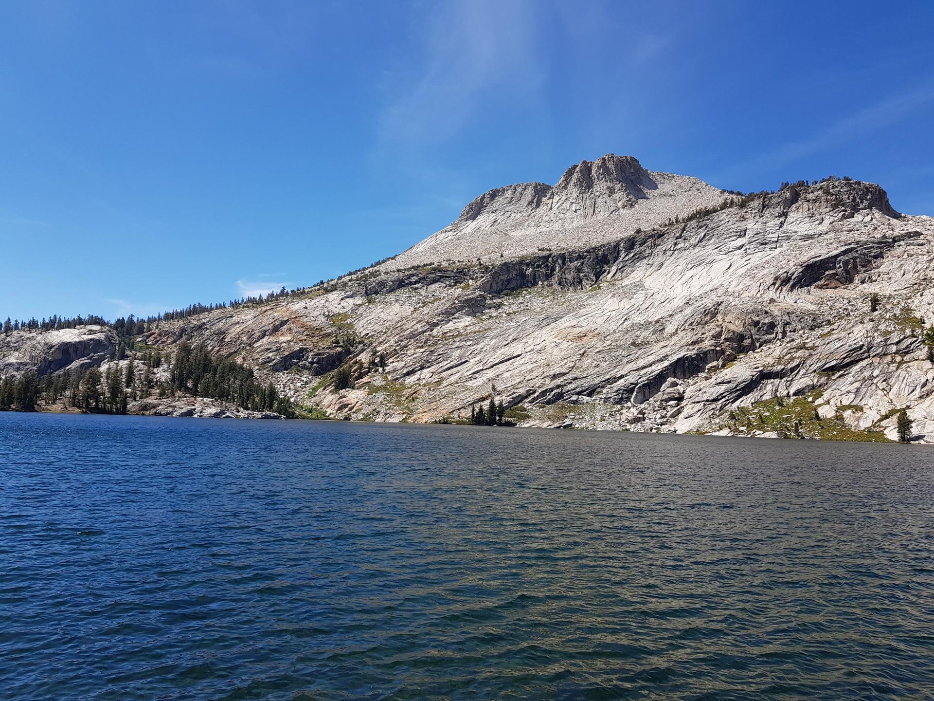 A clear blue lake with a large rocky mountain under a bright sky.