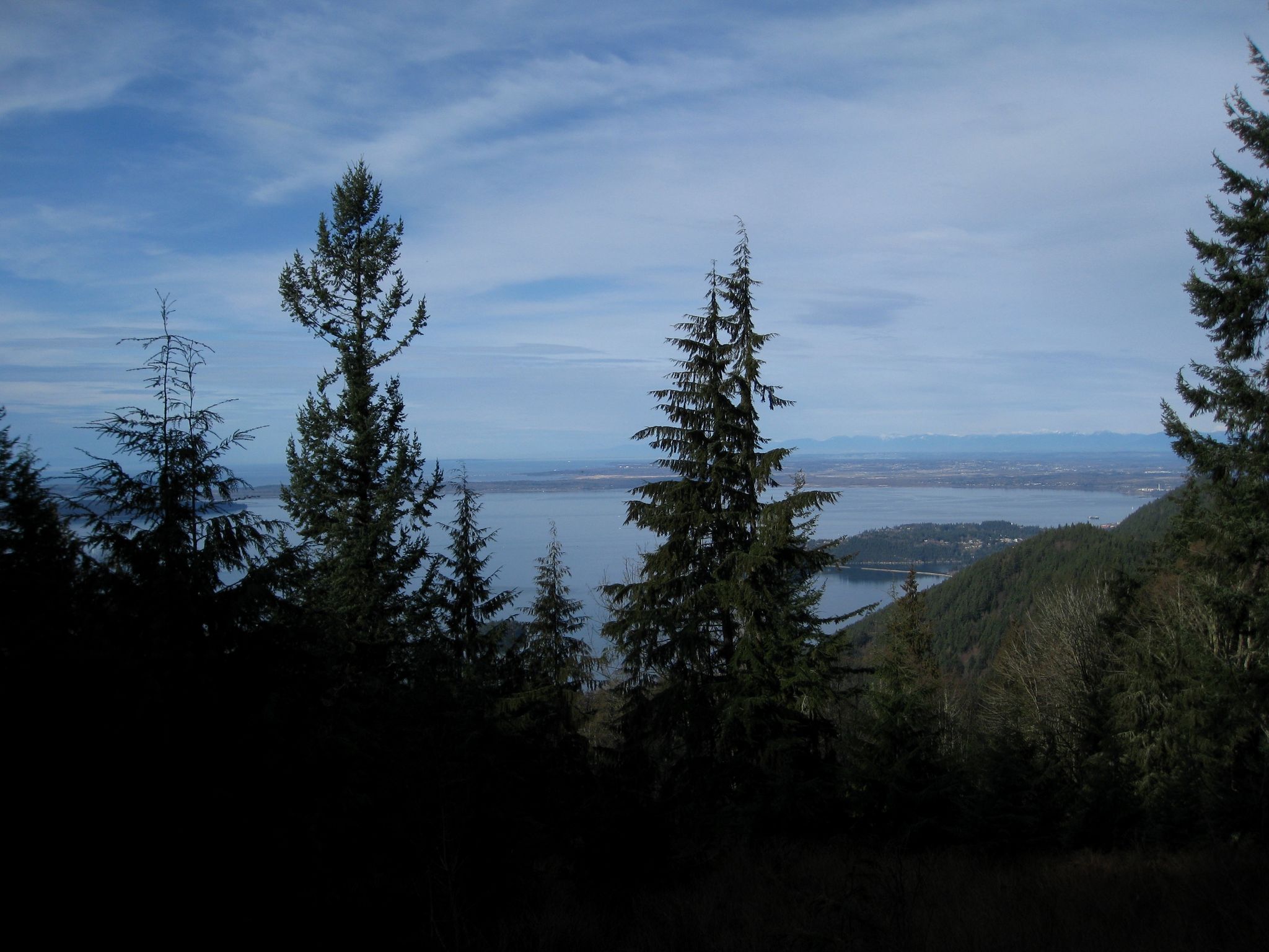 Dark evergreen trees frame a wide body of water under a dramatic sky. - Rock Trail to Lost Lake Loop